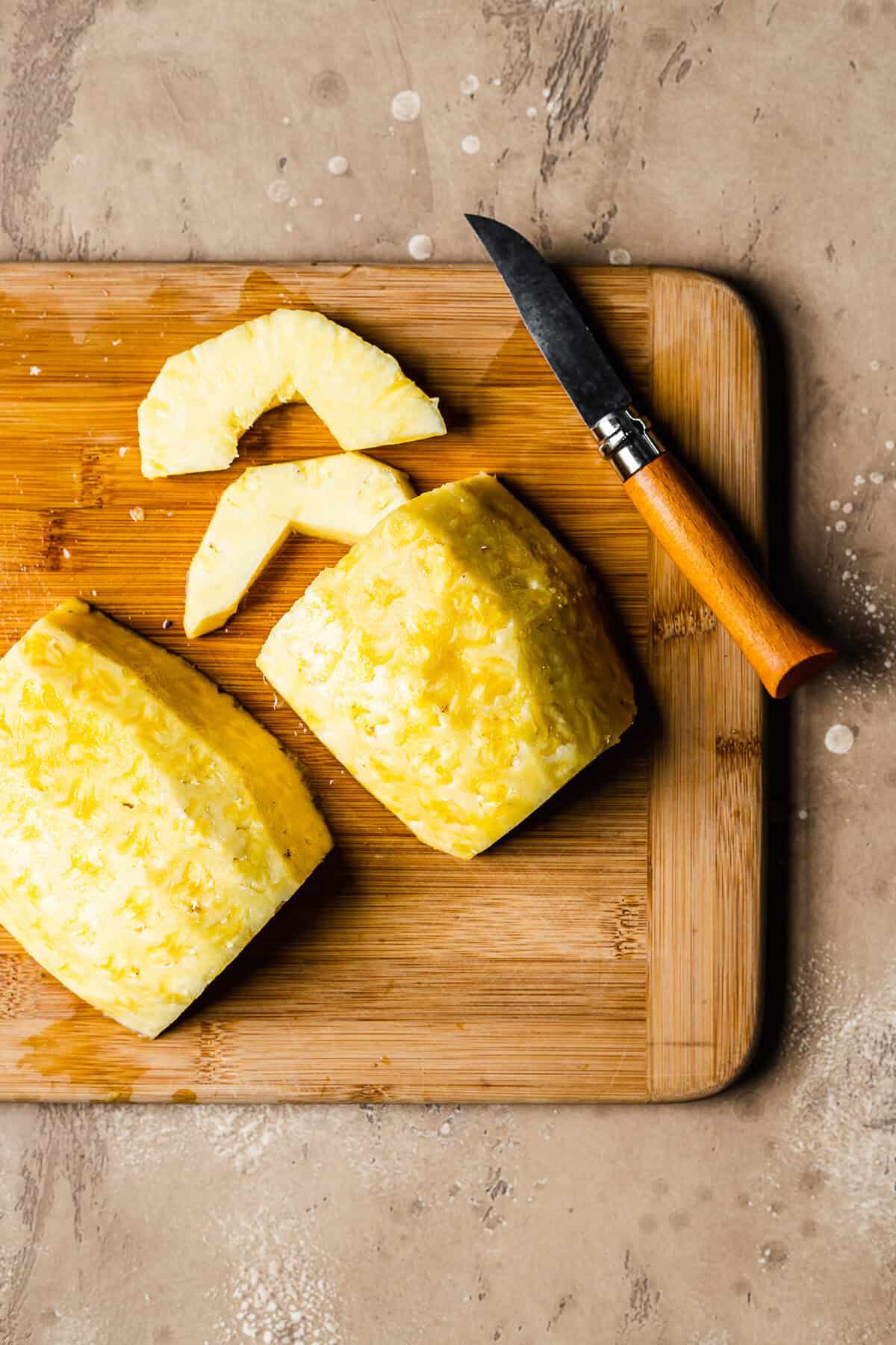 Fresh pineapple cut into slices on a wooden cutting board.