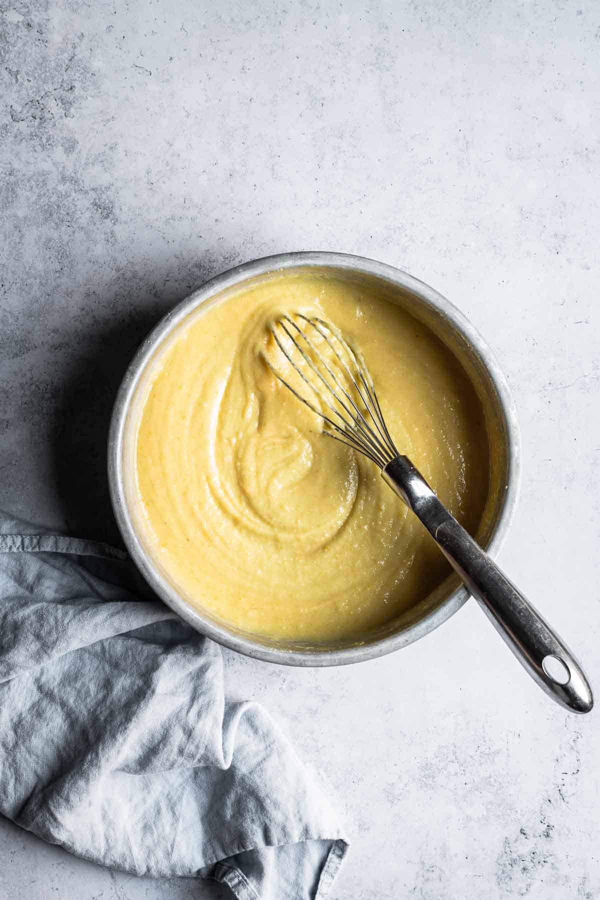 A mixing bowl with pale yellow cake batter swirled with a whisk.