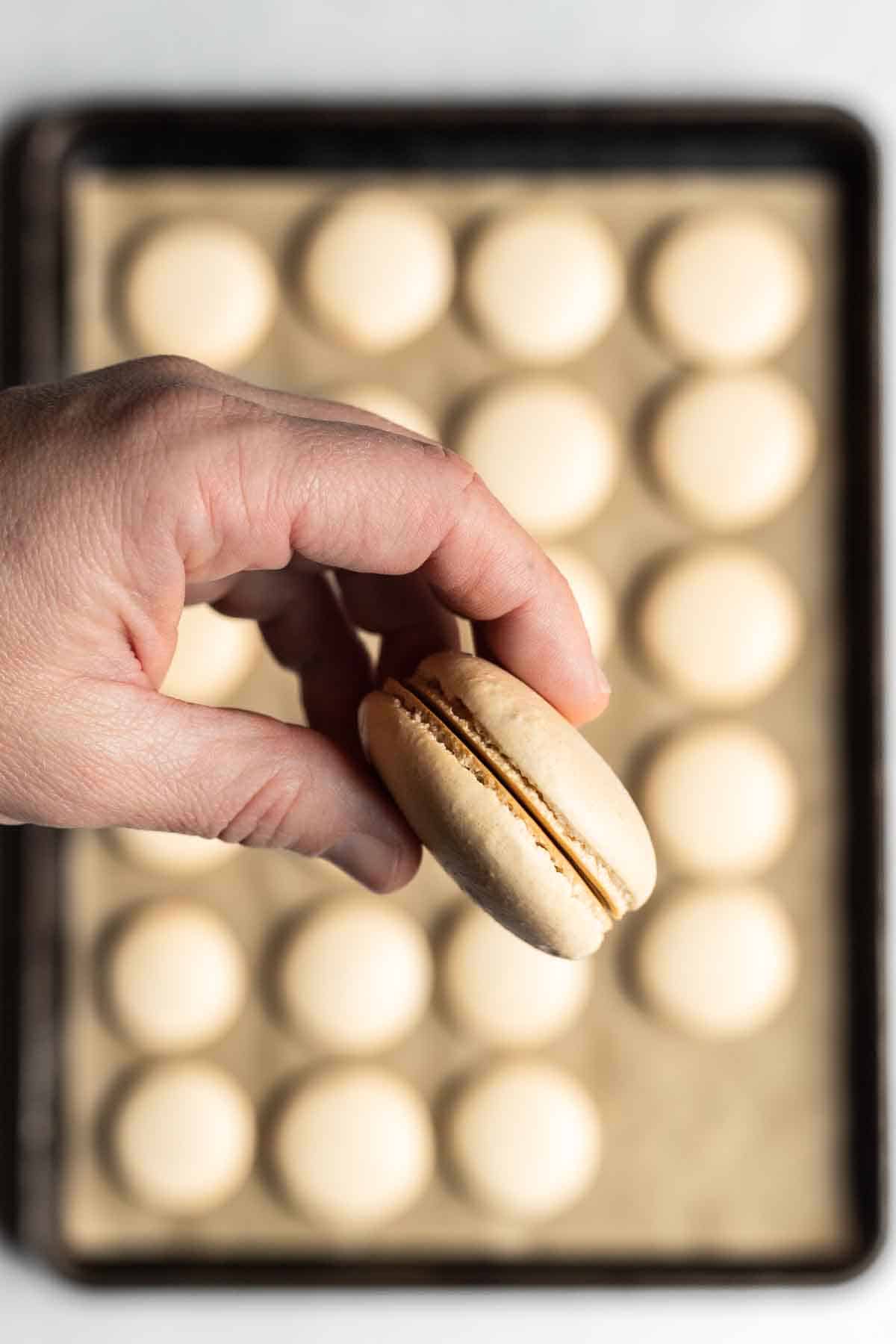 A white skinned hand holding two macaron shells together in a sandwich shape.