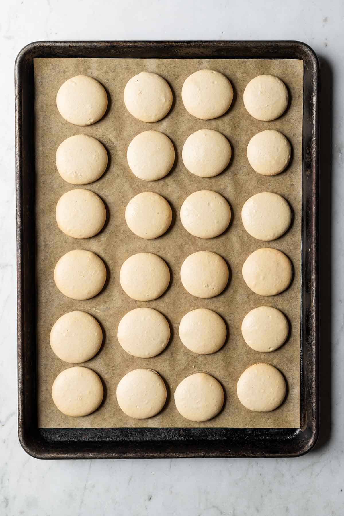 Baked macaron shells on a parchment lined baking sheet.