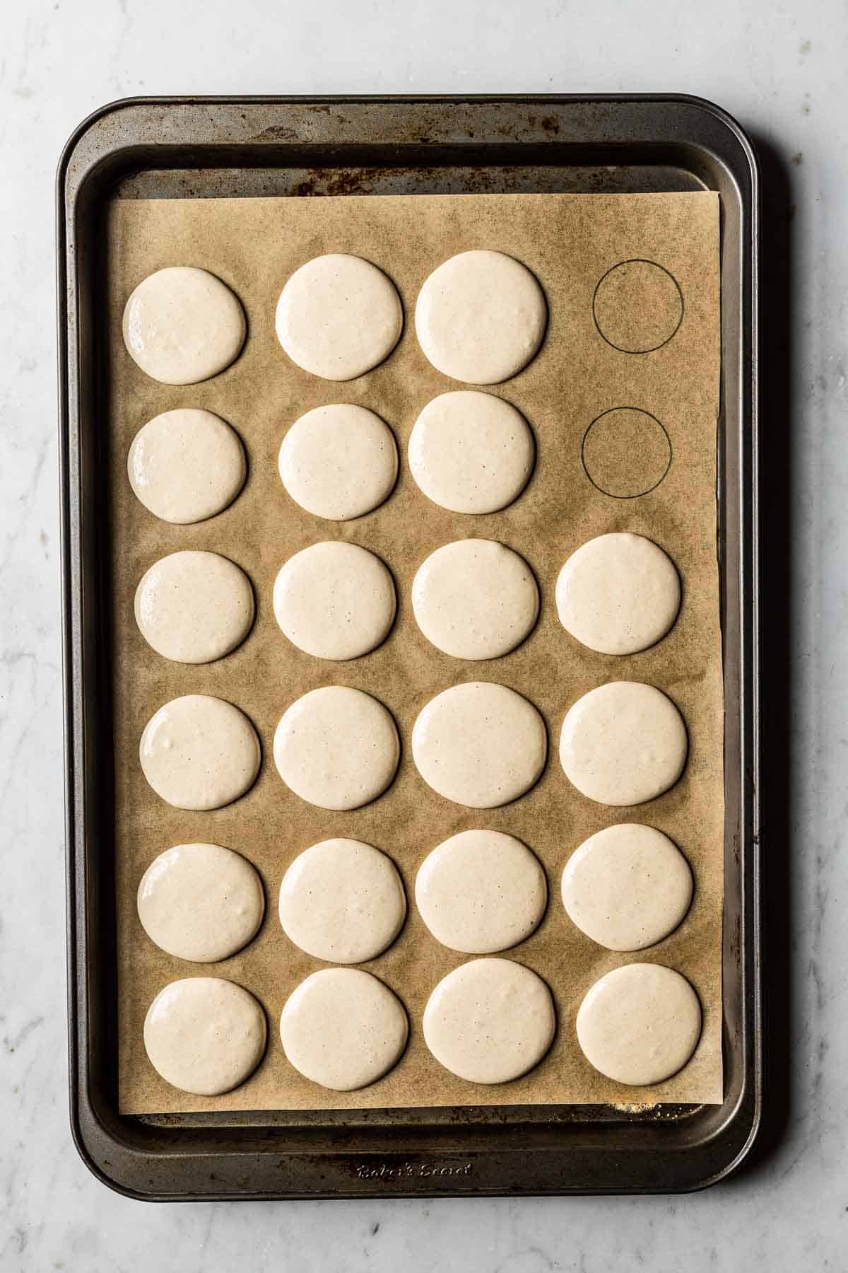 Piped macarons curing on a parchment lined baking sheet.