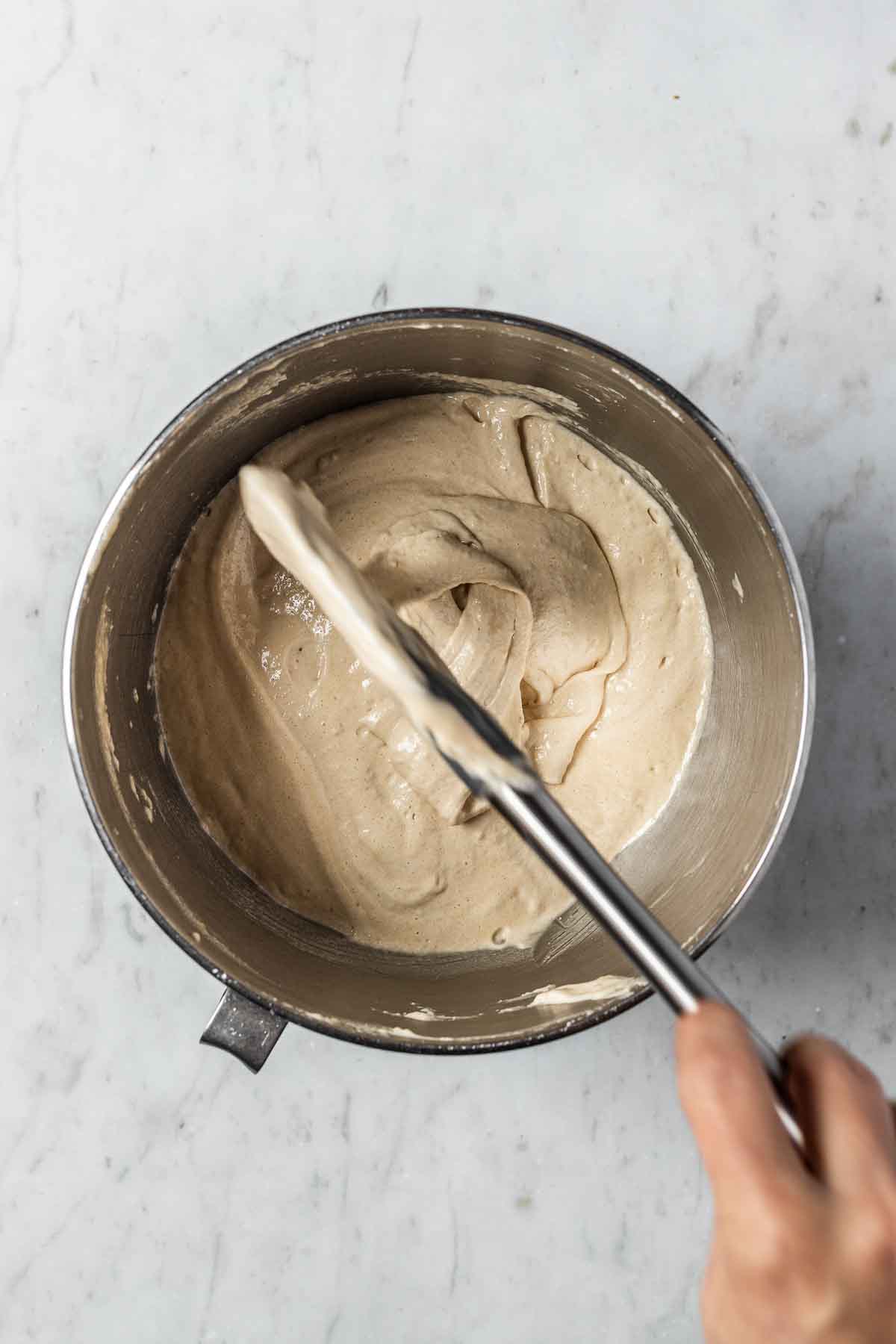 A spatula drizzling finished macaron batter back into the mixing bowl to demonstrate consistency.