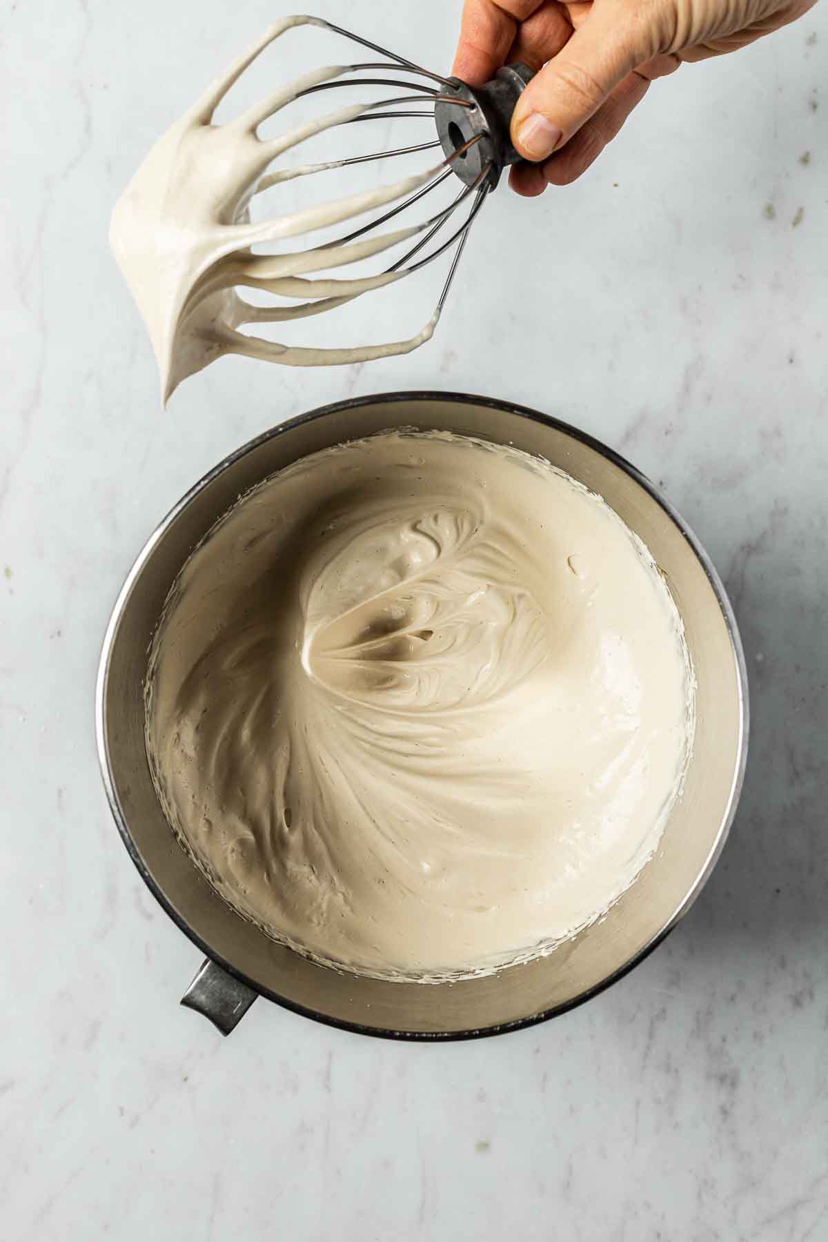 A mixing bowl of stiffly whipped meringue and a whisk showing stiff peaks.