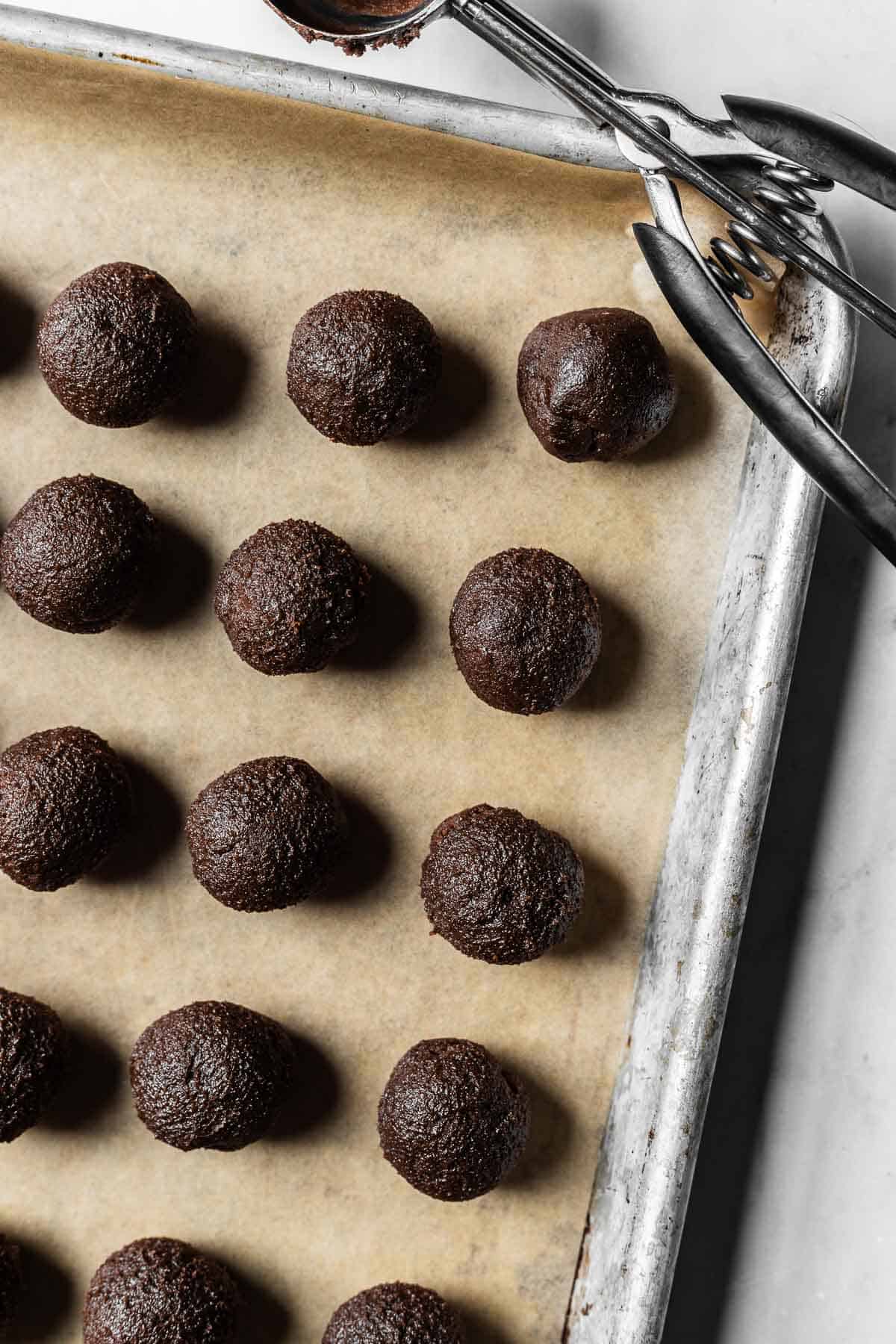Rolled balls of chocolate mascarpone cookie dough on a parchment lined baking sheet.