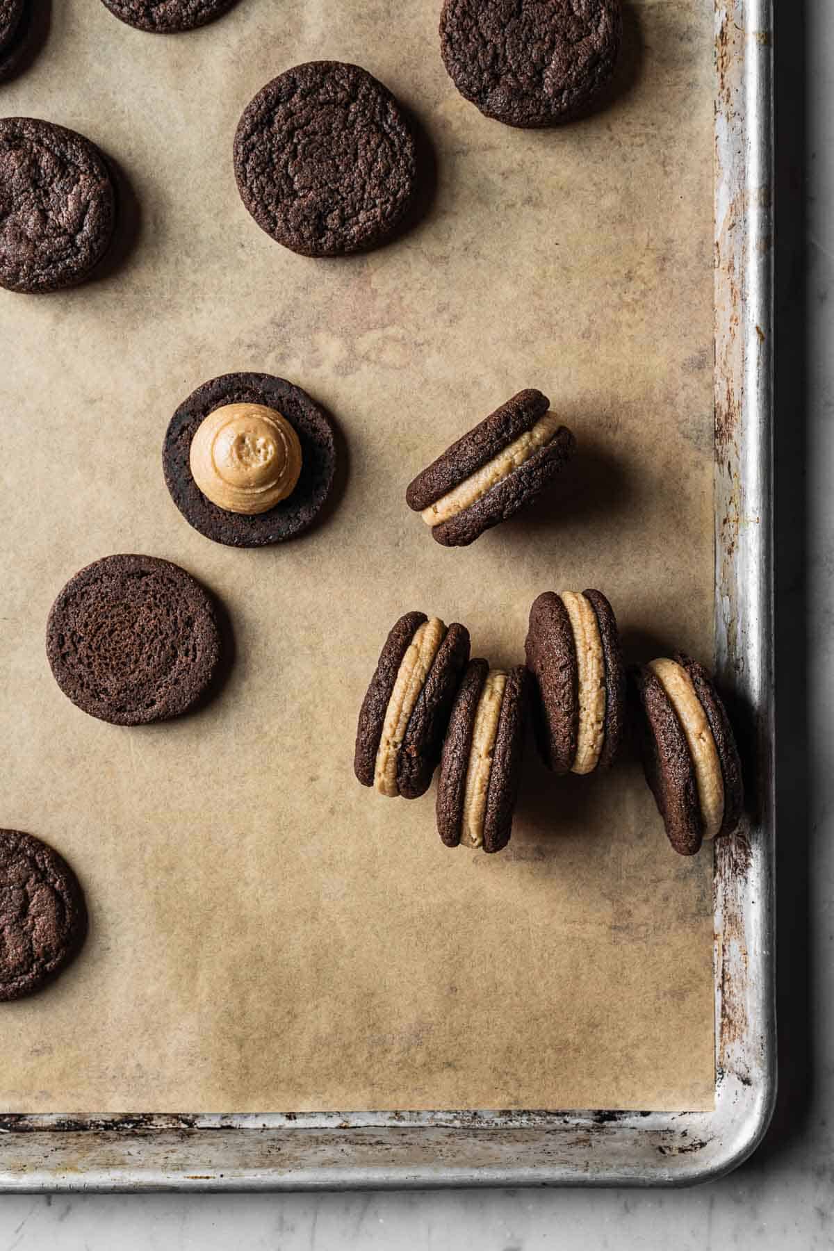 Chocolate cookies filled with coffee mascarpone frosting on a parchment lined baking sheet.