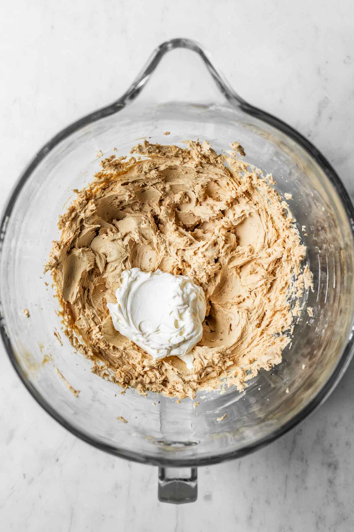 Mascarpone added to coffee buttercream frosting in a glass mixing bowl.