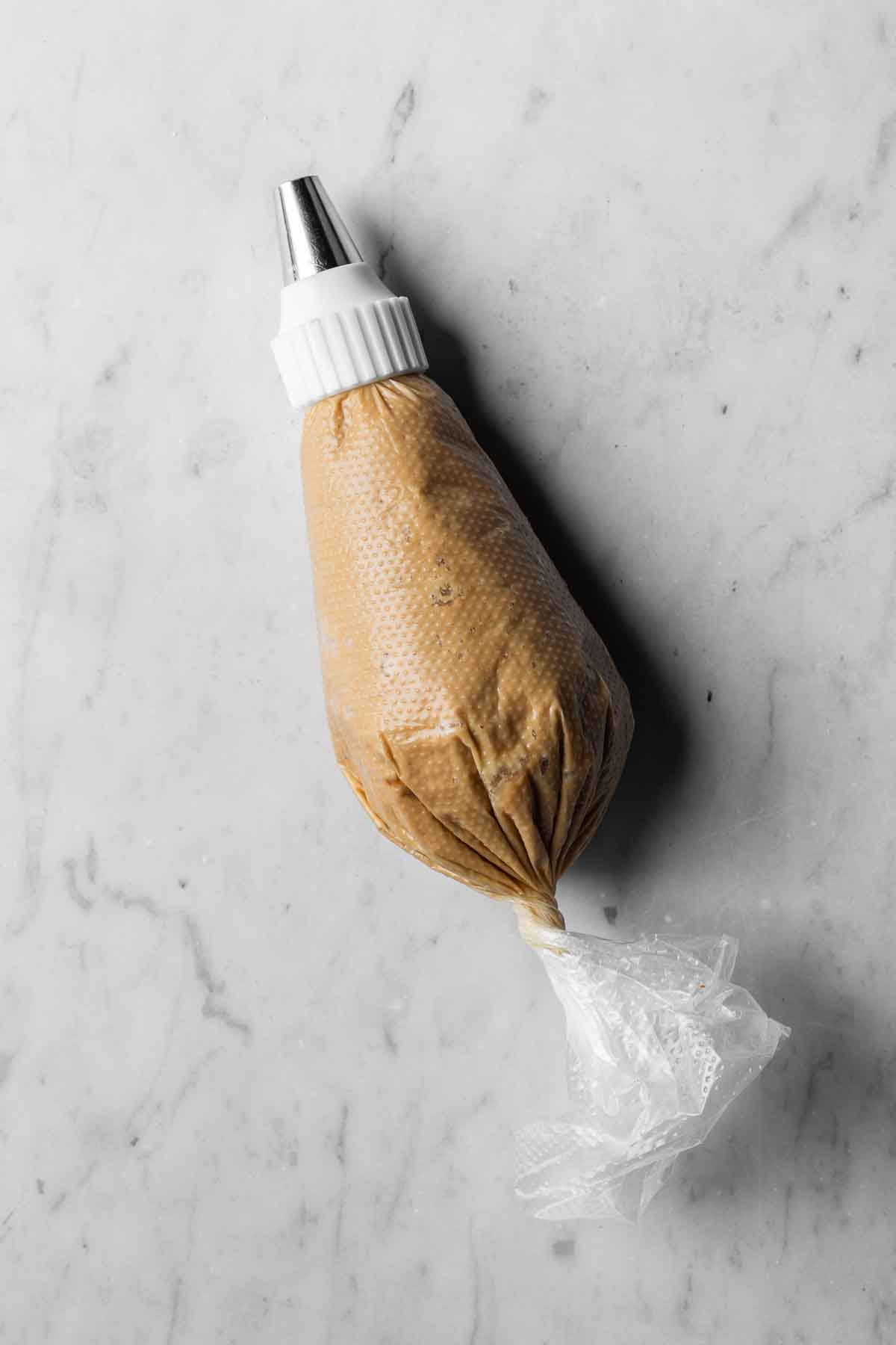 A 16 inch piping bag filled with coffee mascarpone buttercream frosting fitted with a round piping tip.