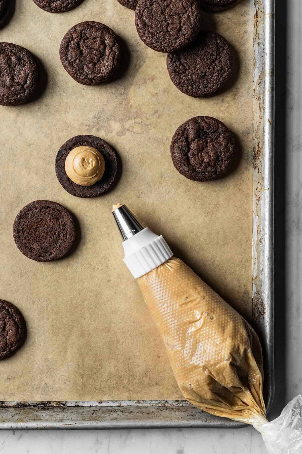 A piping bag of coffee mascarpone frosting and a circle of frosting piped onto a chocolate cookie for sandwich cookies.