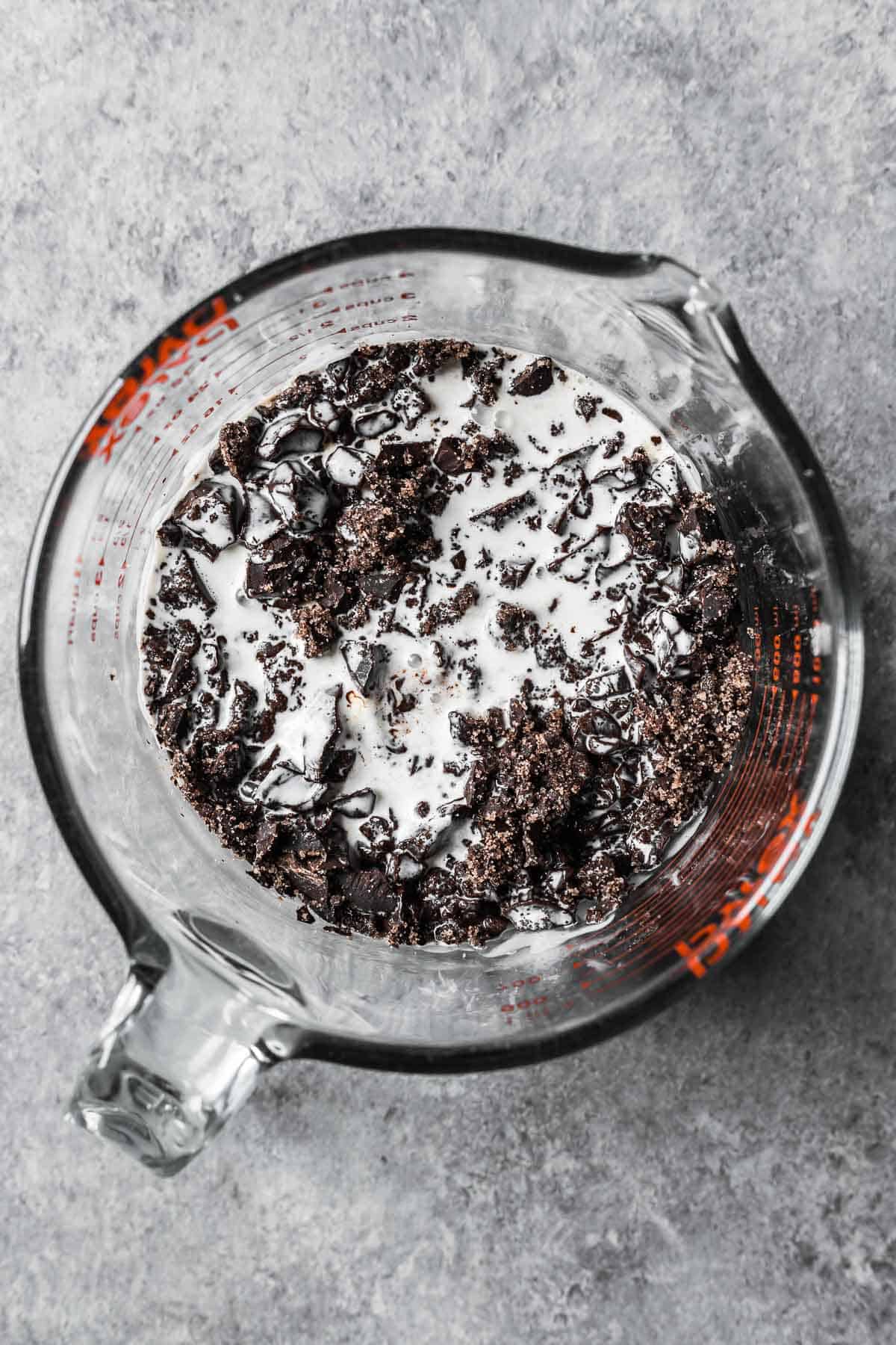 Hot cream poured onto chopped chocolate in a glass measuring container.