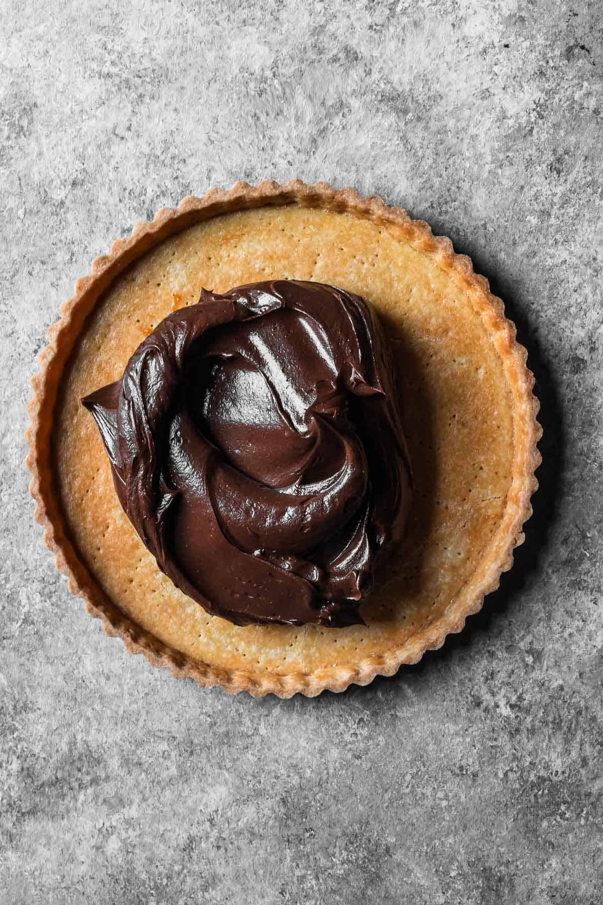 A blind baked tart shell with a chocolate mascarpone ganache filling before being spread.