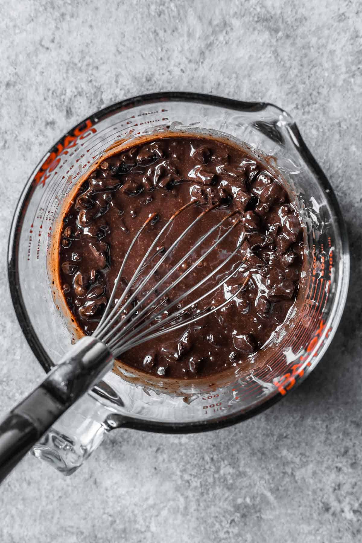 Partially melted chocolate chunks in hot cream in a glass mixing container.