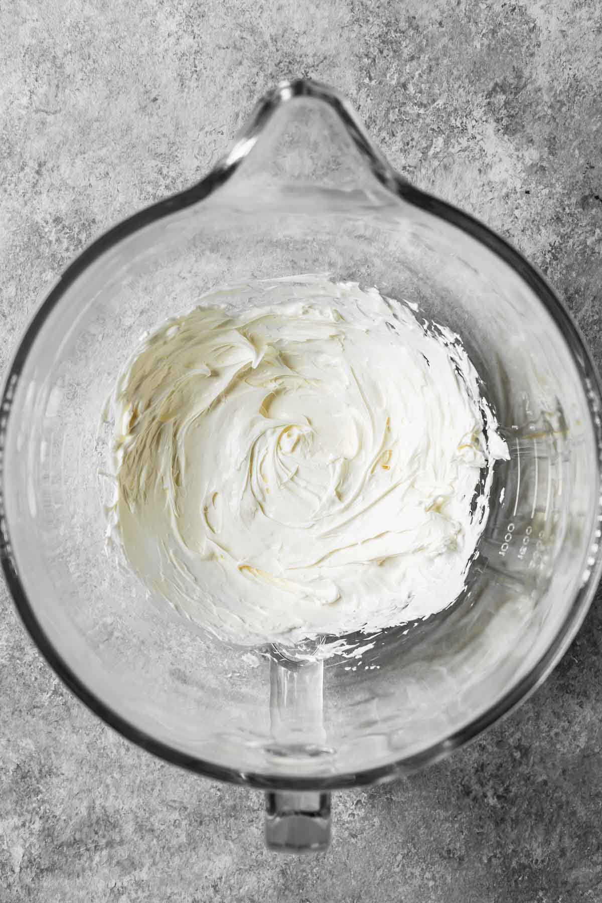 Lightly beaten mascarpone cheese in a large glass mixing bowl.