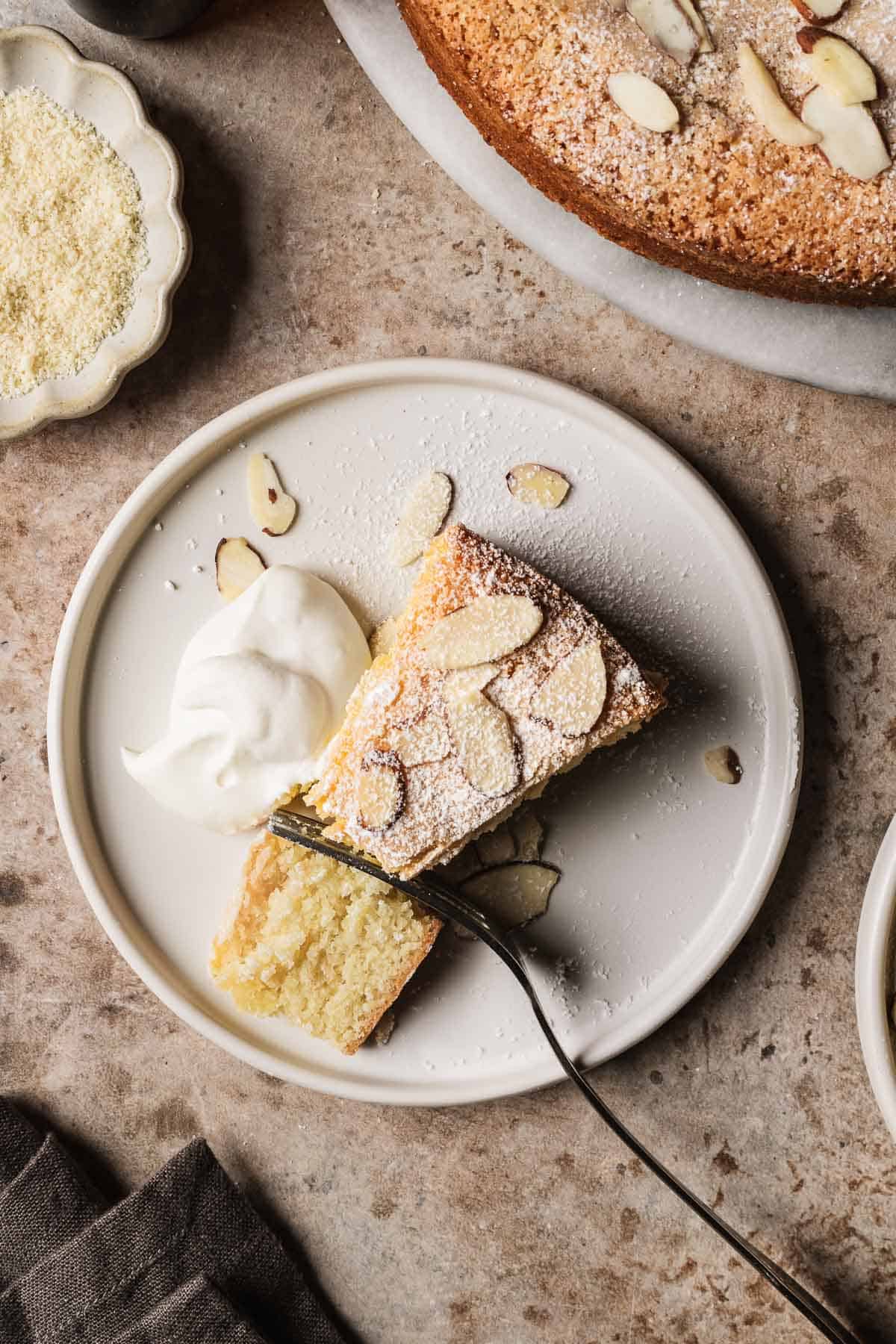 A slice of cake dusted with powdered sugar and slivered almonds on a white ceramic plate.