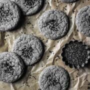 Cookies sprinkled with black sesame seeds on a parchment paper lined baking sheet.
