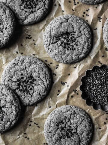 Cookies sprinkled with black sesame seeds on a parchment paper lined baking sheet.