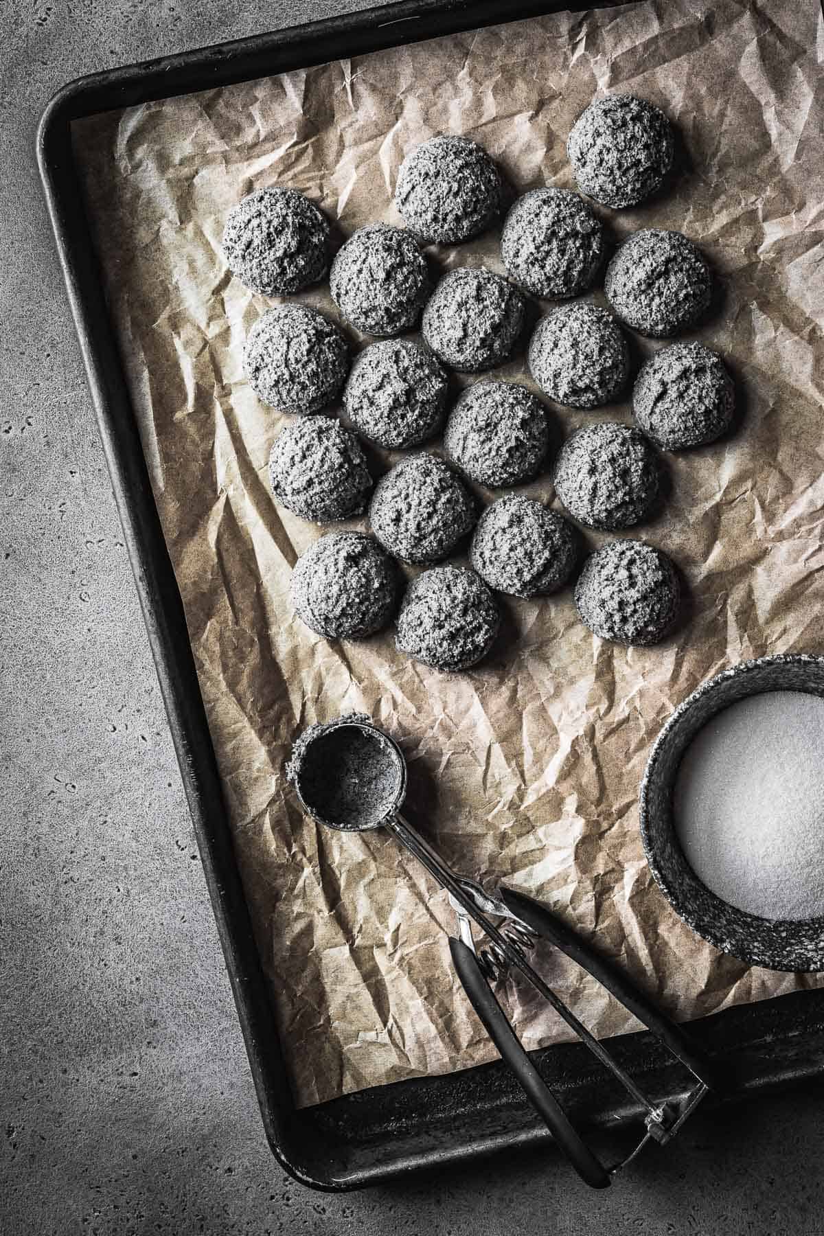 Scoops of grey cookie dough on a parchment lined baking sheet.