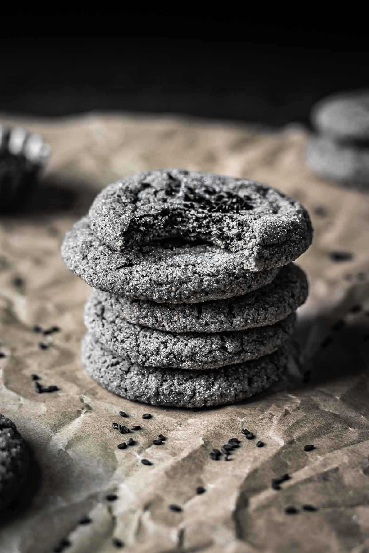 A side view of 5 stacked black sesame cookies with a bite taken out of the top cookie showing the texture of the interior.