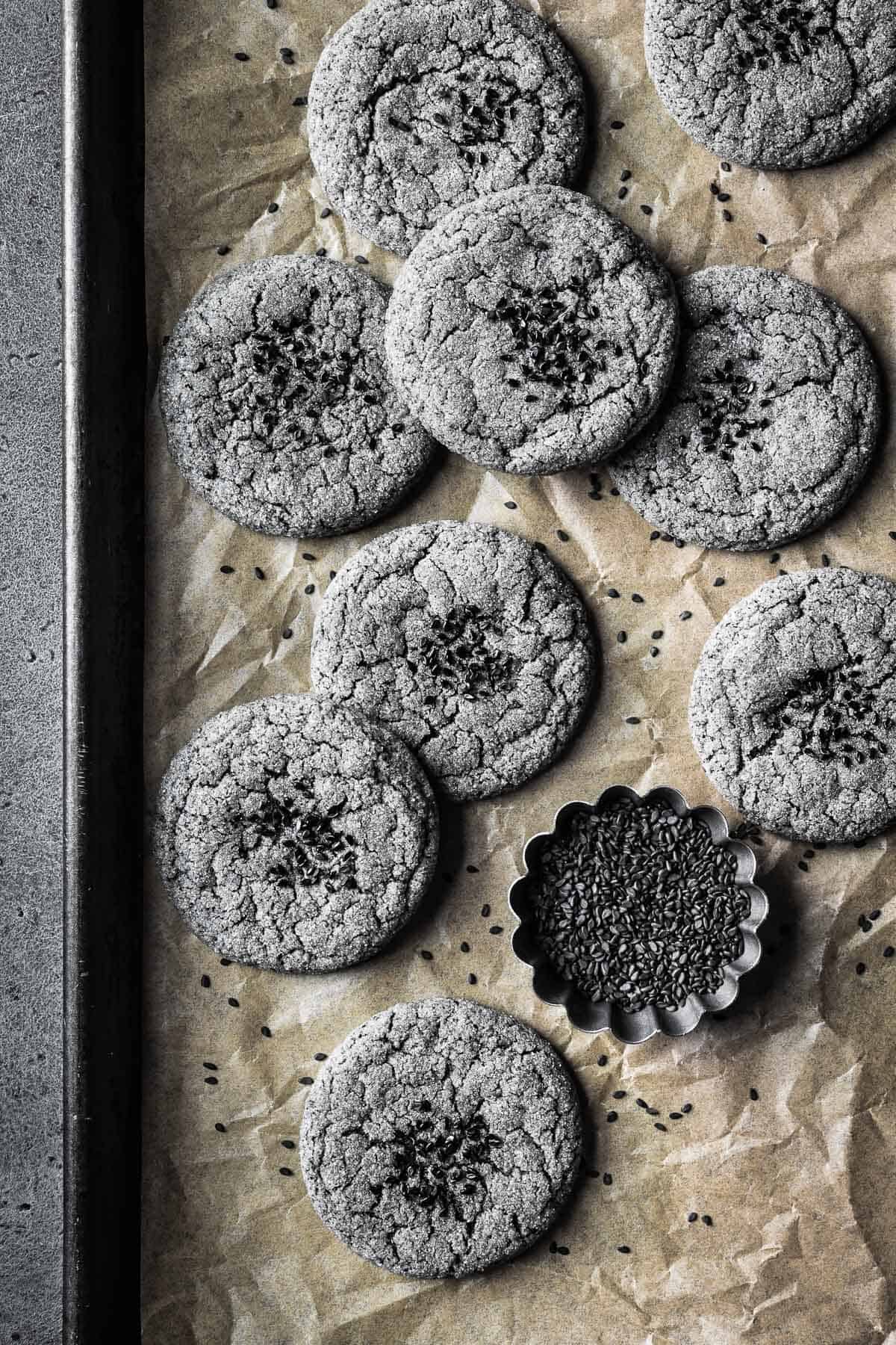 Cookies sprinkled with black sesame seeds on a parchment paper lined baking sheet.
