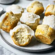 Lemon poppy seed muffins on a ceramic plate with a large bite taken out of a muffin in the foreground, showing the crumb and poppy seeds inside.