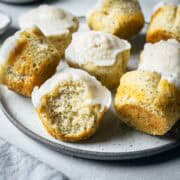 Lemon poppy seed muffins on a ceramic plate with a large bite taken out of a muffin in the foreground, showing the crumb and poppy seeds inside.
