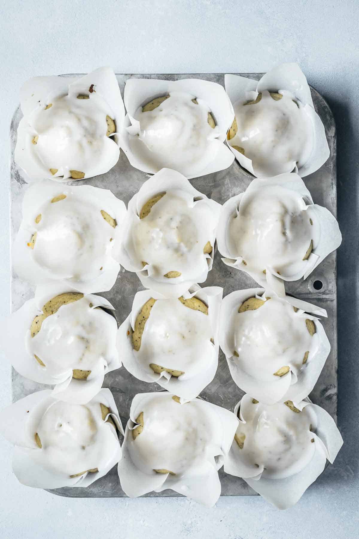 Baked muffins with white glaze on top in white parchment paper liners.