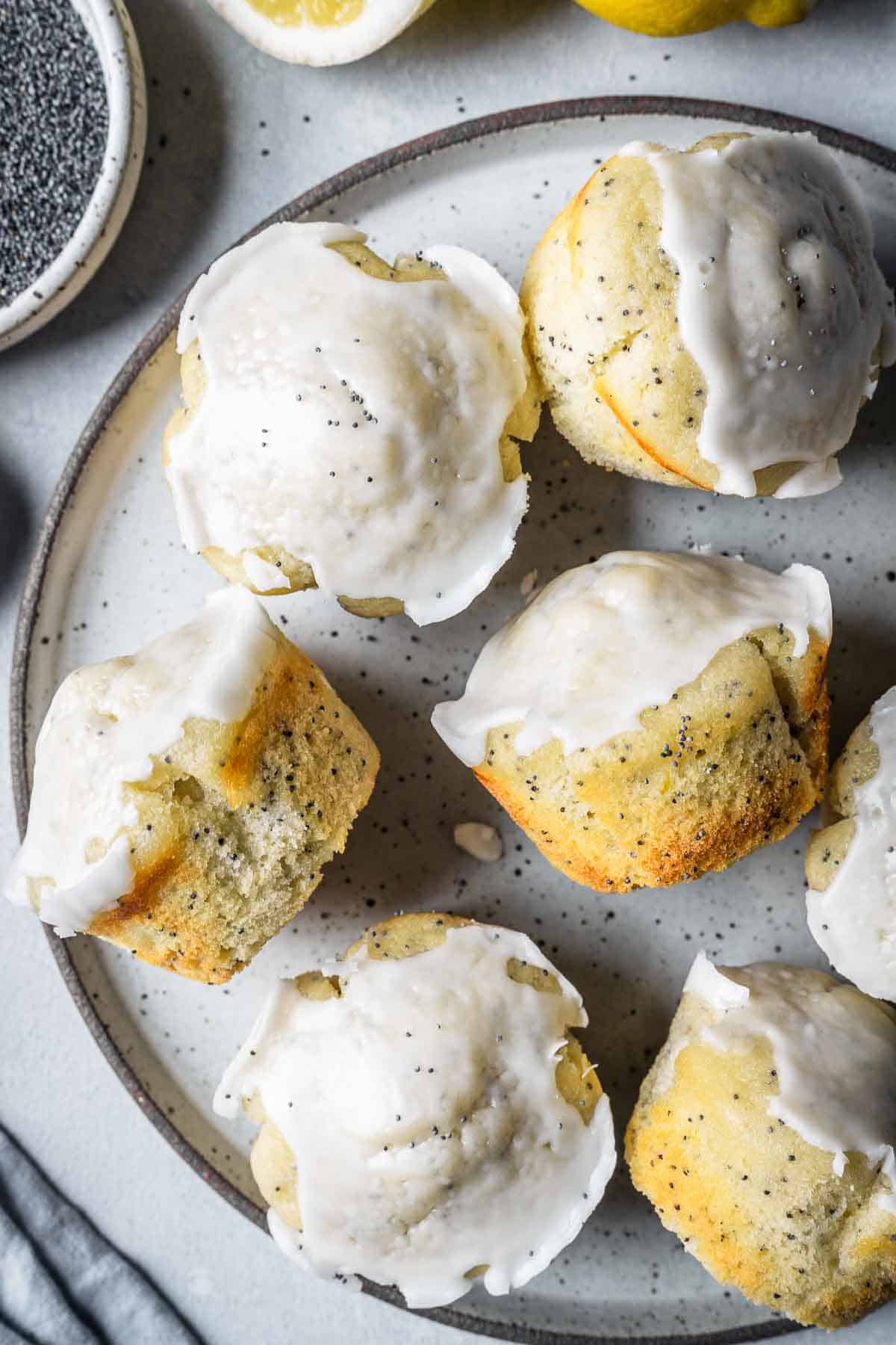 Lemon poppy seed muffins topped with glaze on a plate with some muffins tipped to the side to show the crumb and golden color.