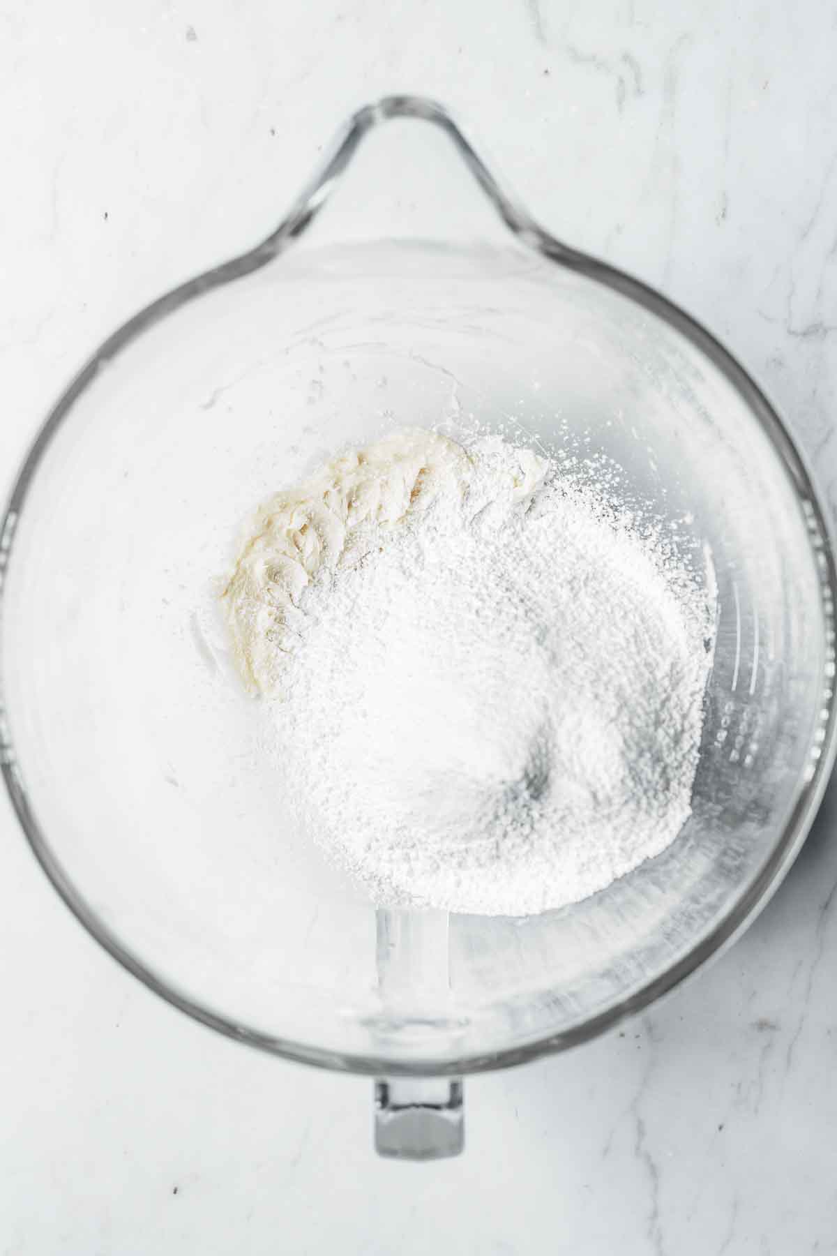 Powdered sugar and cornstarch added to wet ingredients in a glass mixing bowl.