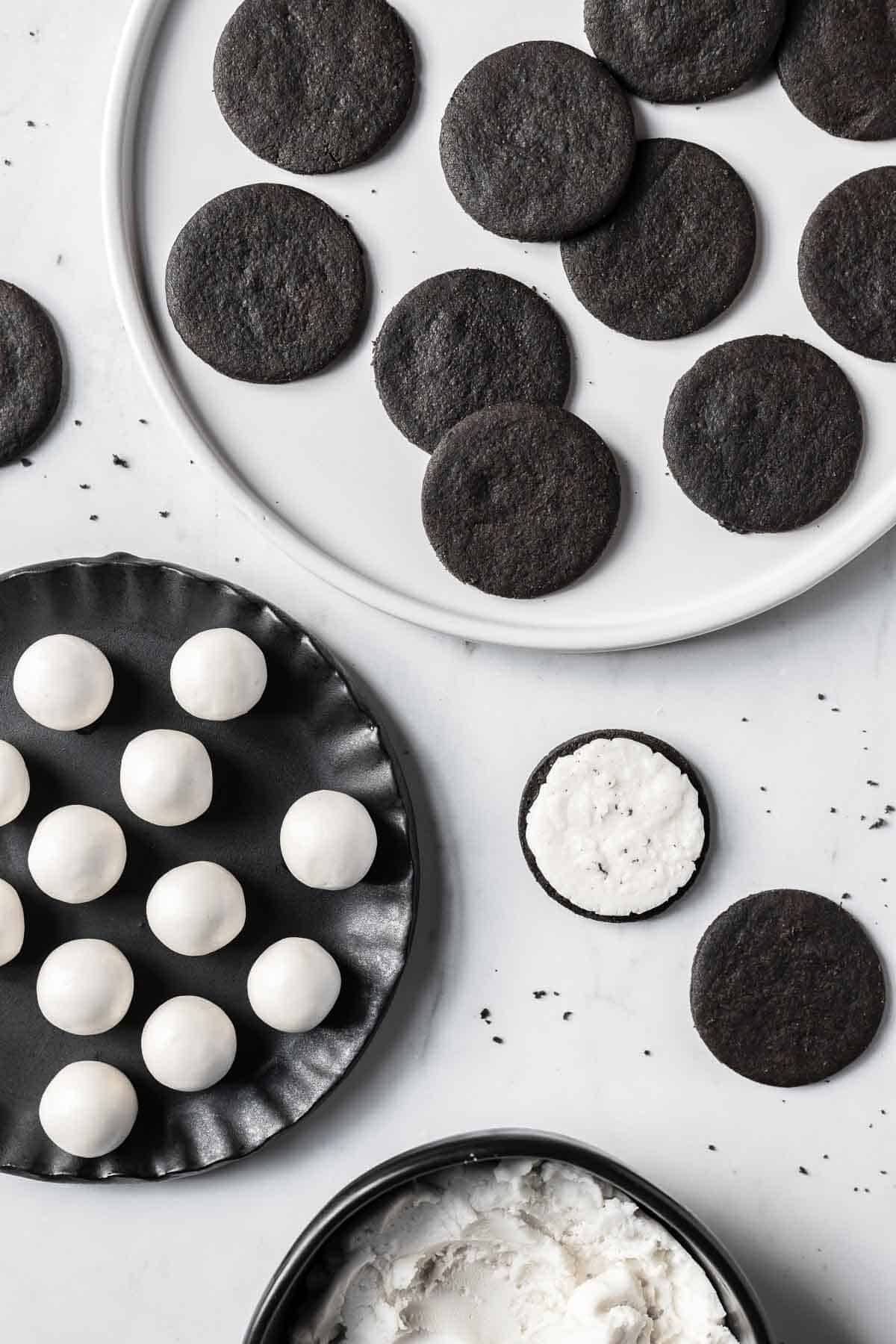 Balls of filling on a black plate surrounded by a bowl of filling and a plate of cookies.