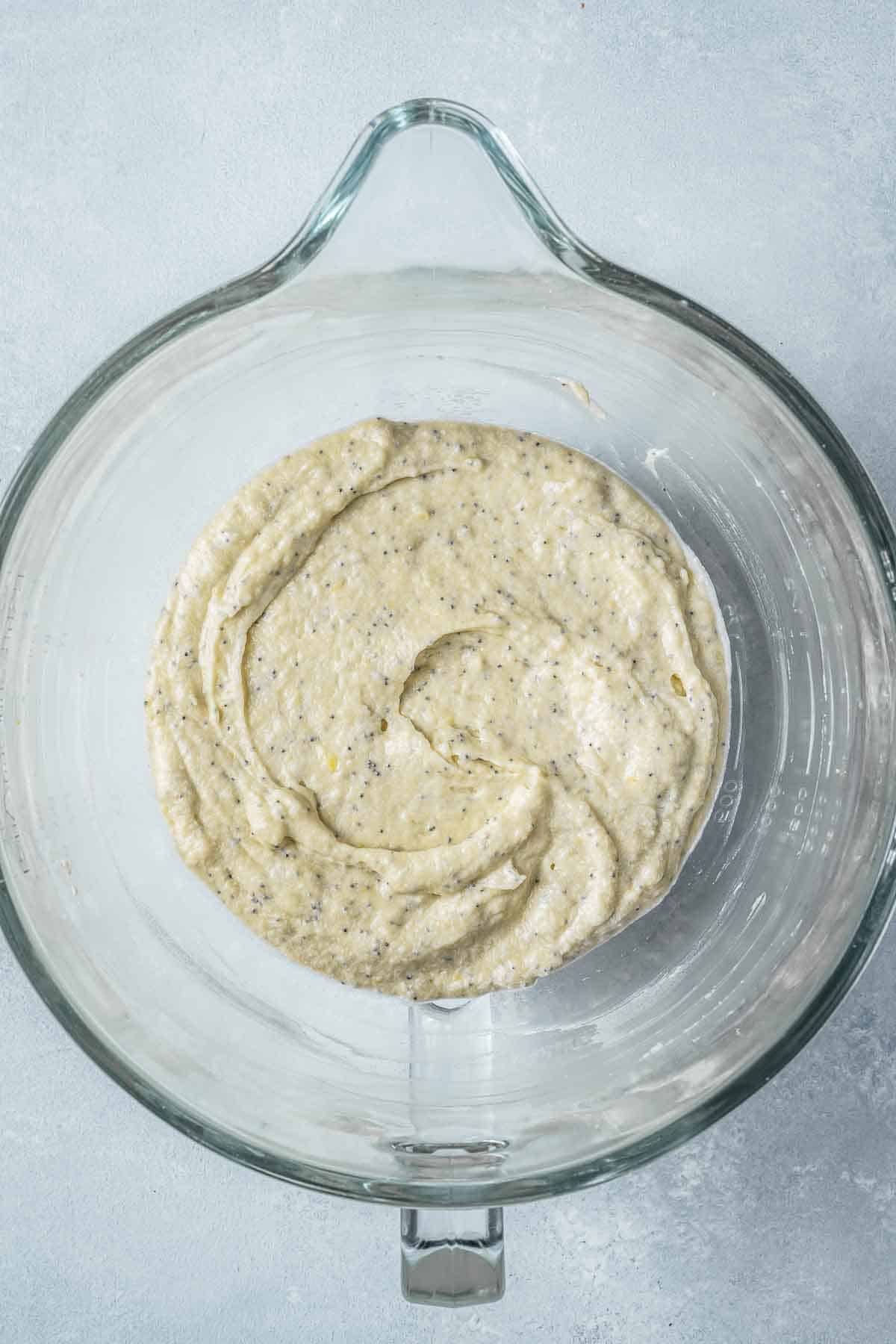 Batter for lemon poppy seed muffins in a clear glass mixing bowl.