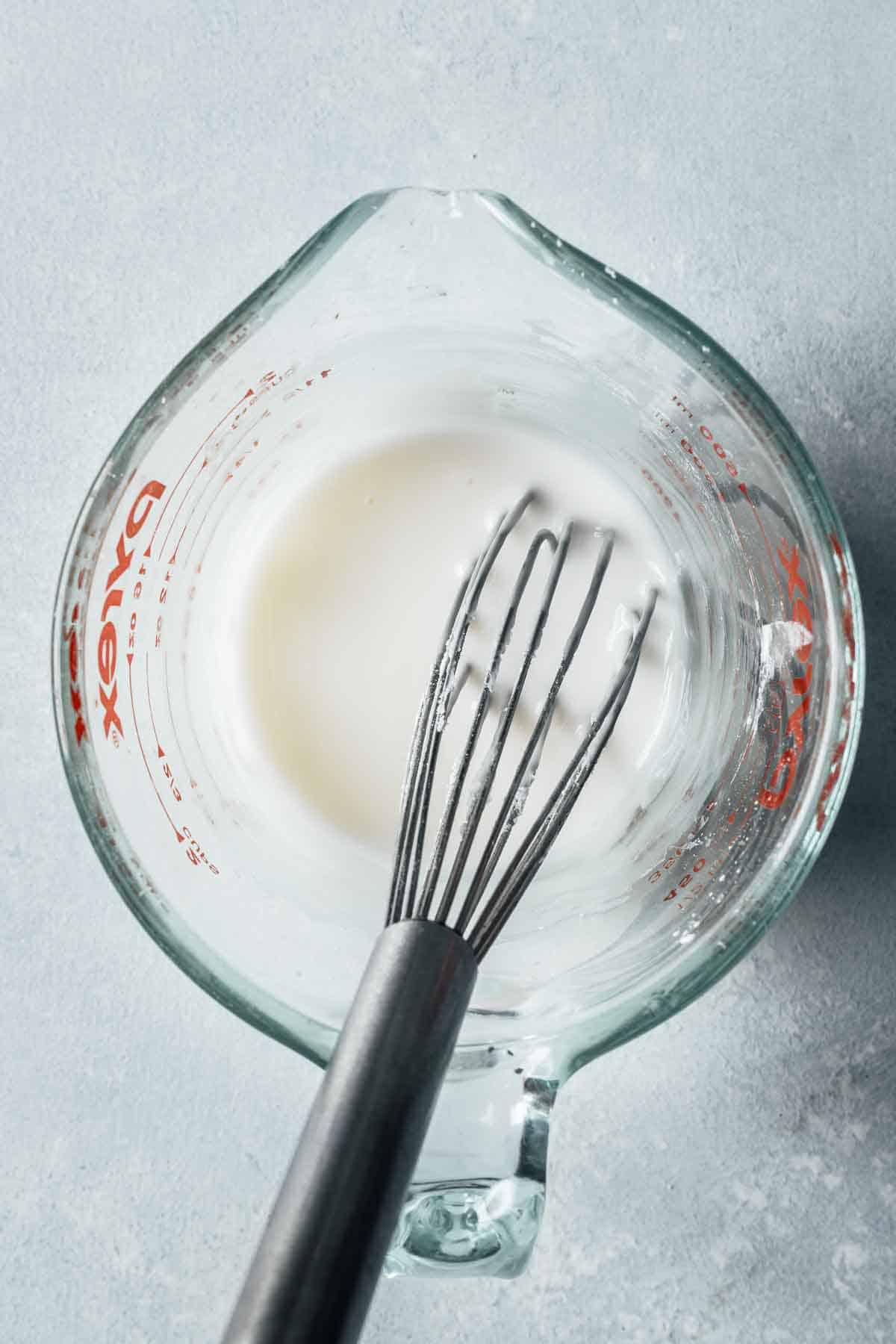 White glaze in a glass measuring cup with a whisk.