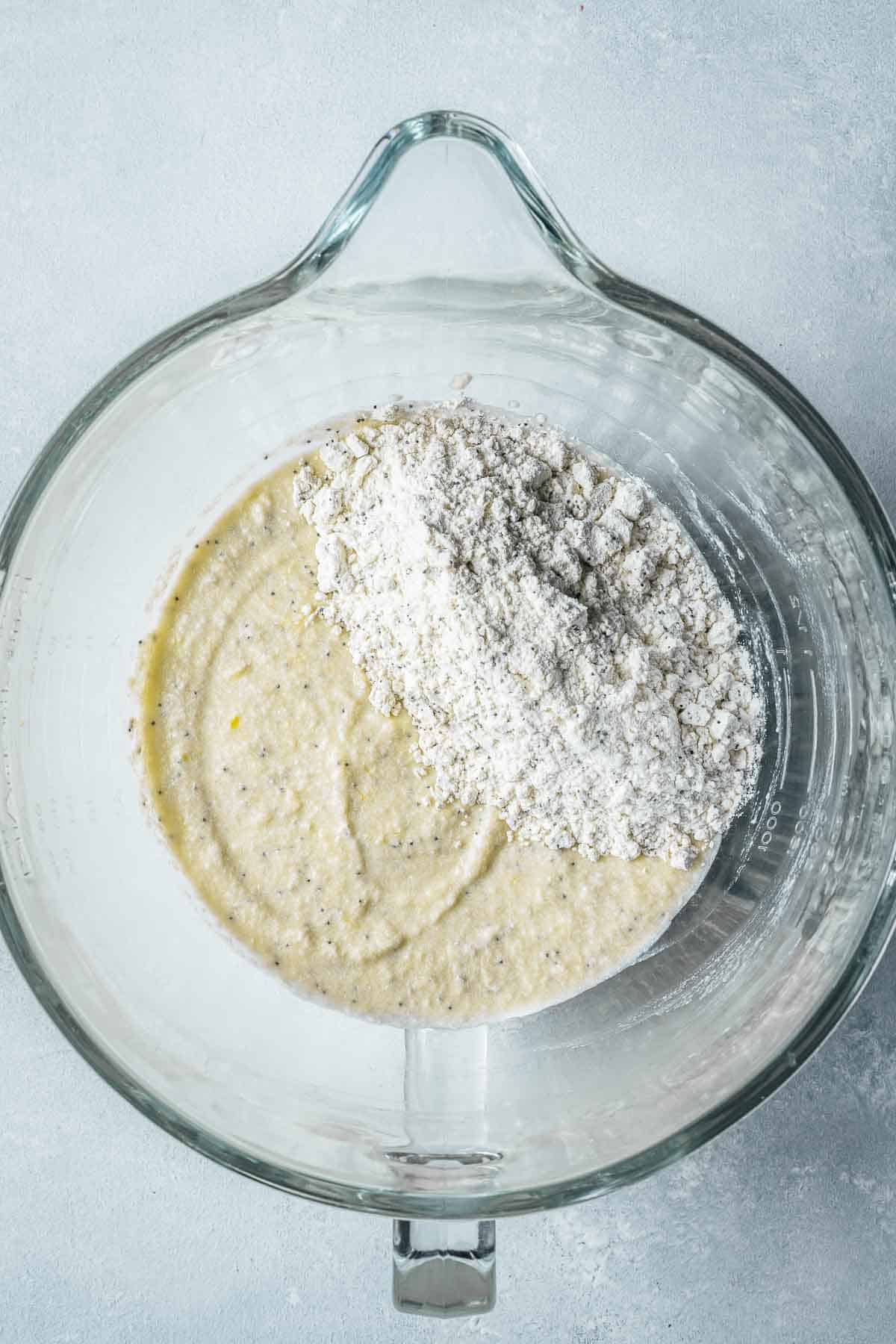 Dry ingredients on top of wet batter in a clear glass mixing bowl.