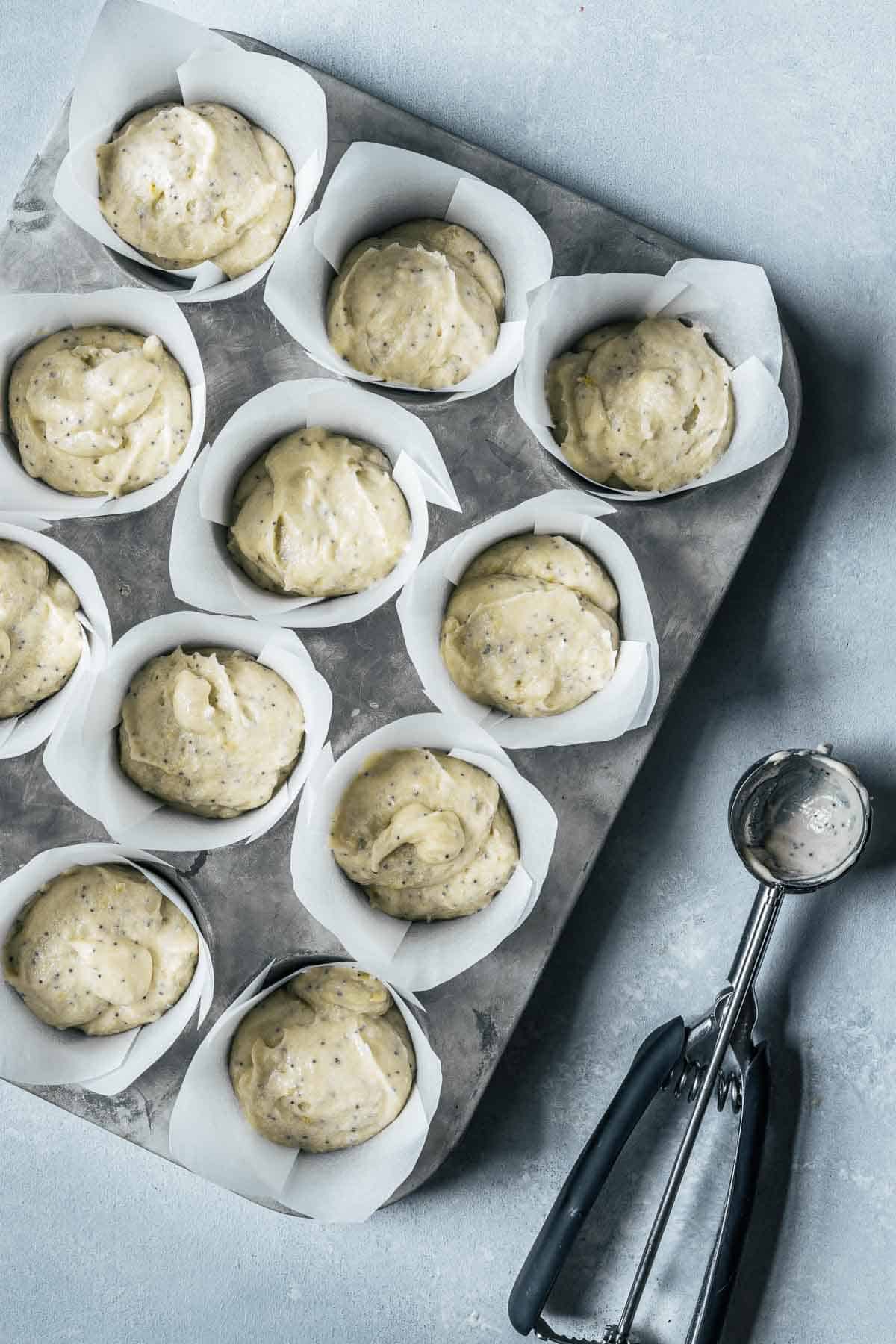 Muffin batter scooped into paper liners in a metal muffin tin.