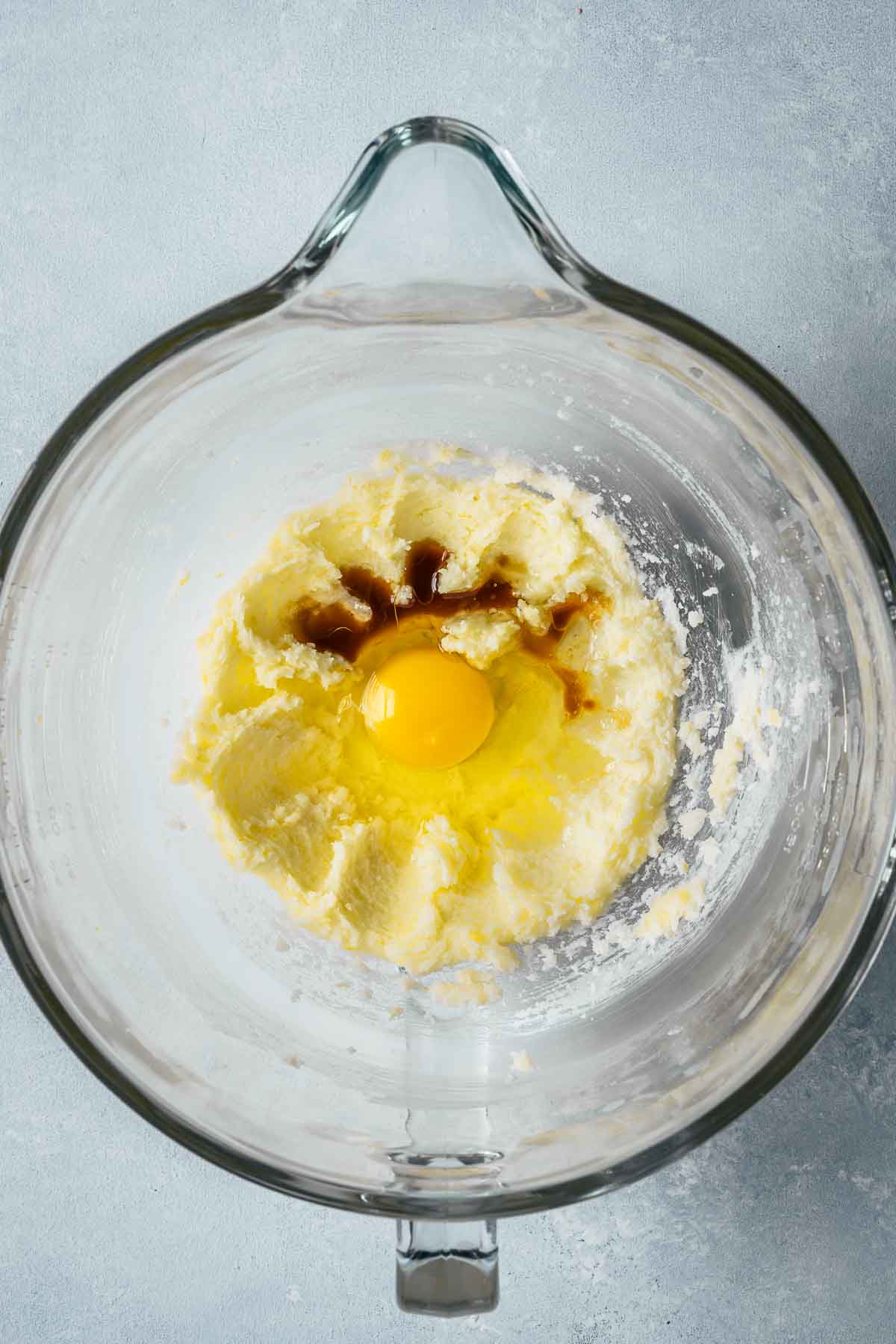 Eggs and extracts added to creamed butter and sugar in a clear glass mixing bowl.