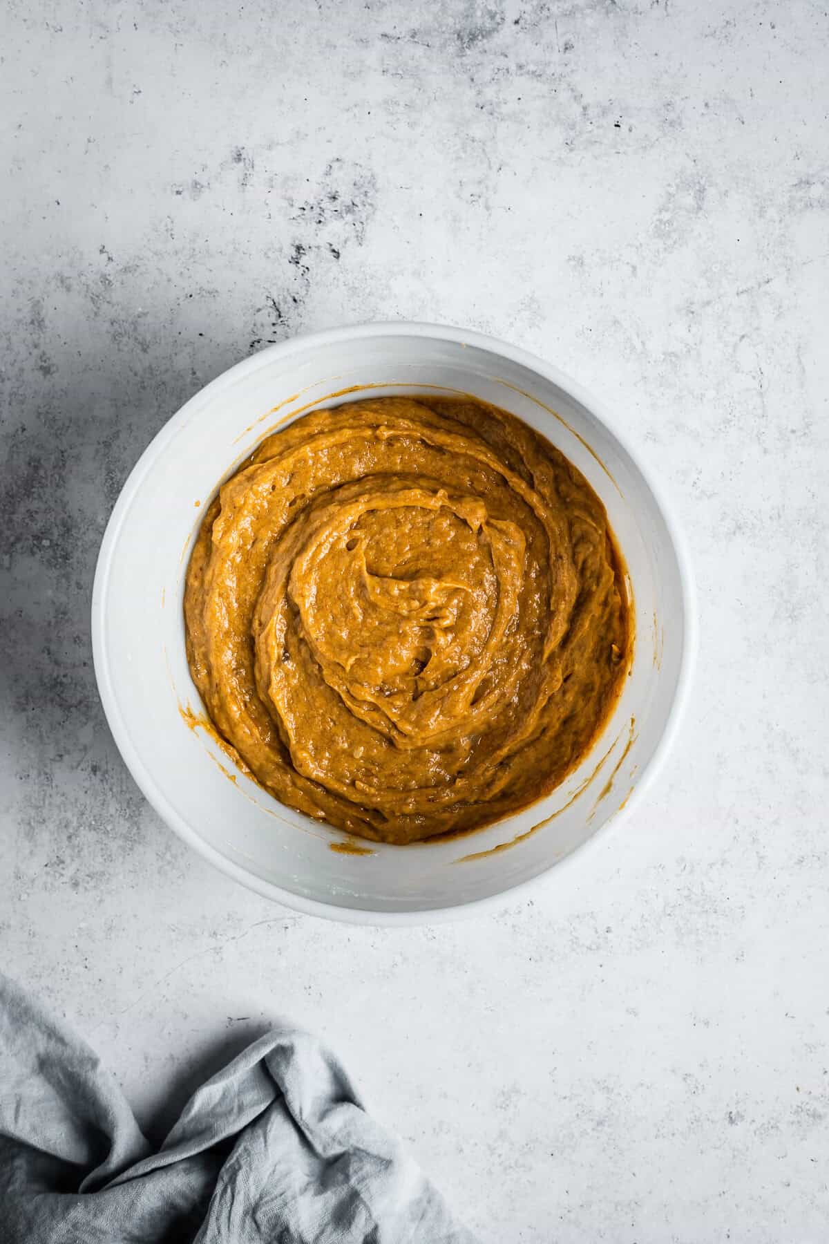 Batter for pumpkin muffins in a white glass mixing bowl.