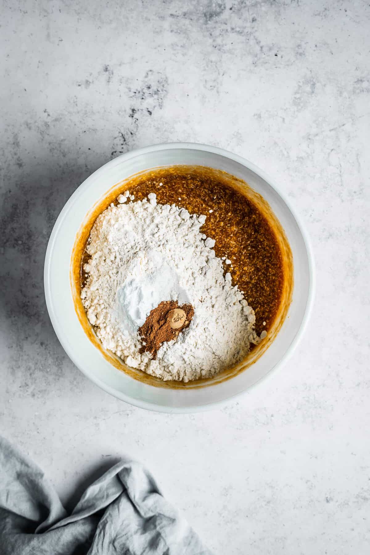 Dry ingredients added to muffin batter in a white glass mixing bowl.