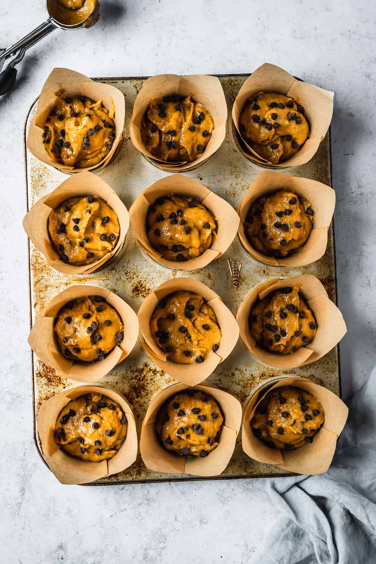 Muffin batter scooped into parchment paper cups in a metal tin.