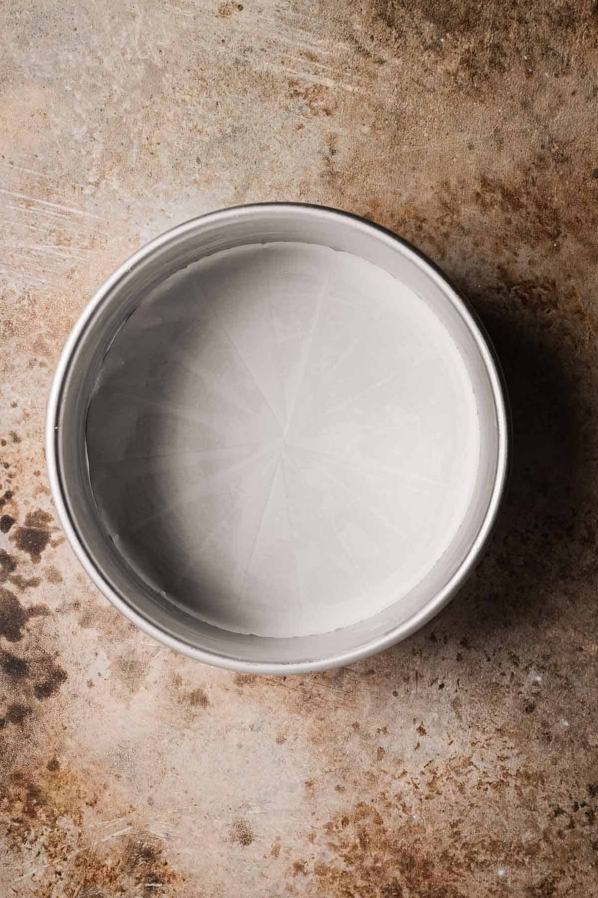 A greased and parchment lined 8 inch round metal baking pan.
