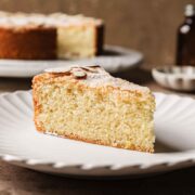 A slice of cake dusted with powdered sugar and slivered almonds on a white plate.