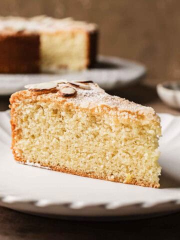 A slice of cake dusted with powdered sugar and slivered almonds on a white plate.