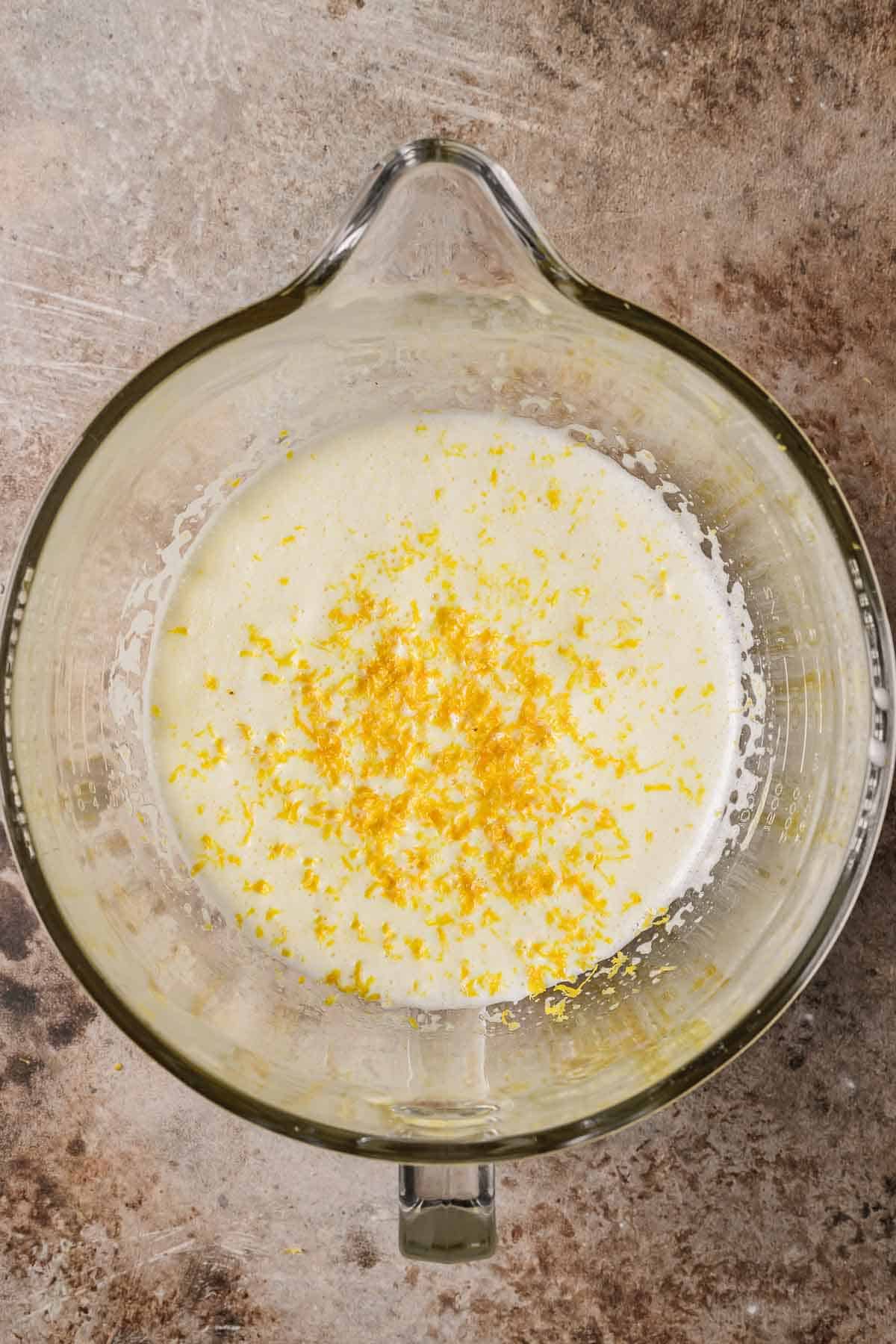 Lemon zest and almond extract added to beaten egg mixture in a glass mixing bowl.