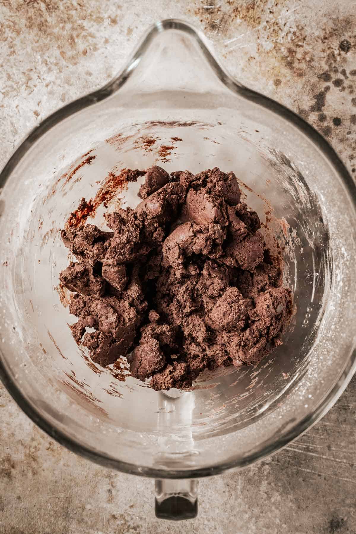 Fully mixed chocolate cookie dough in a clear glass mixing bowl.
