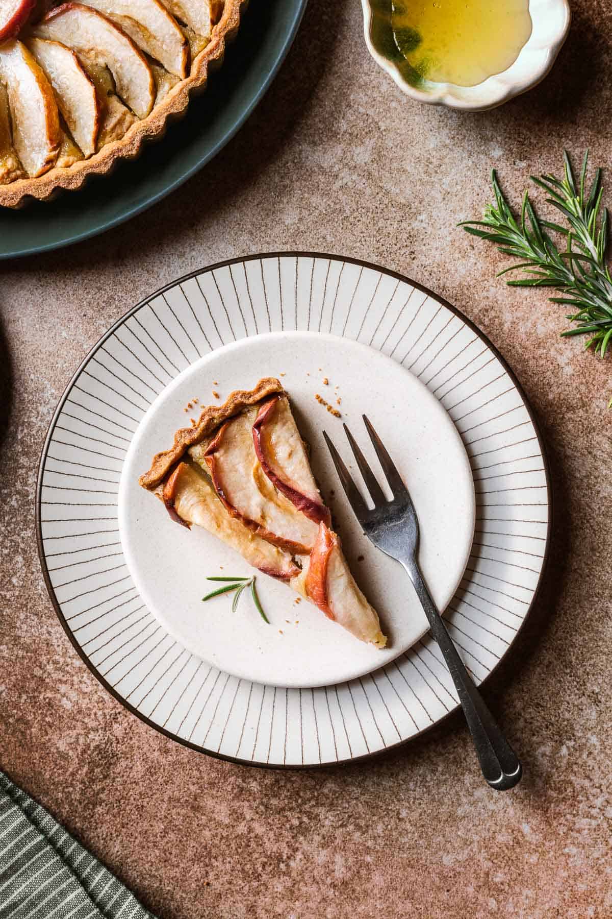 A slice of apple tart on a tan plate with a radial striped plate underneath.
