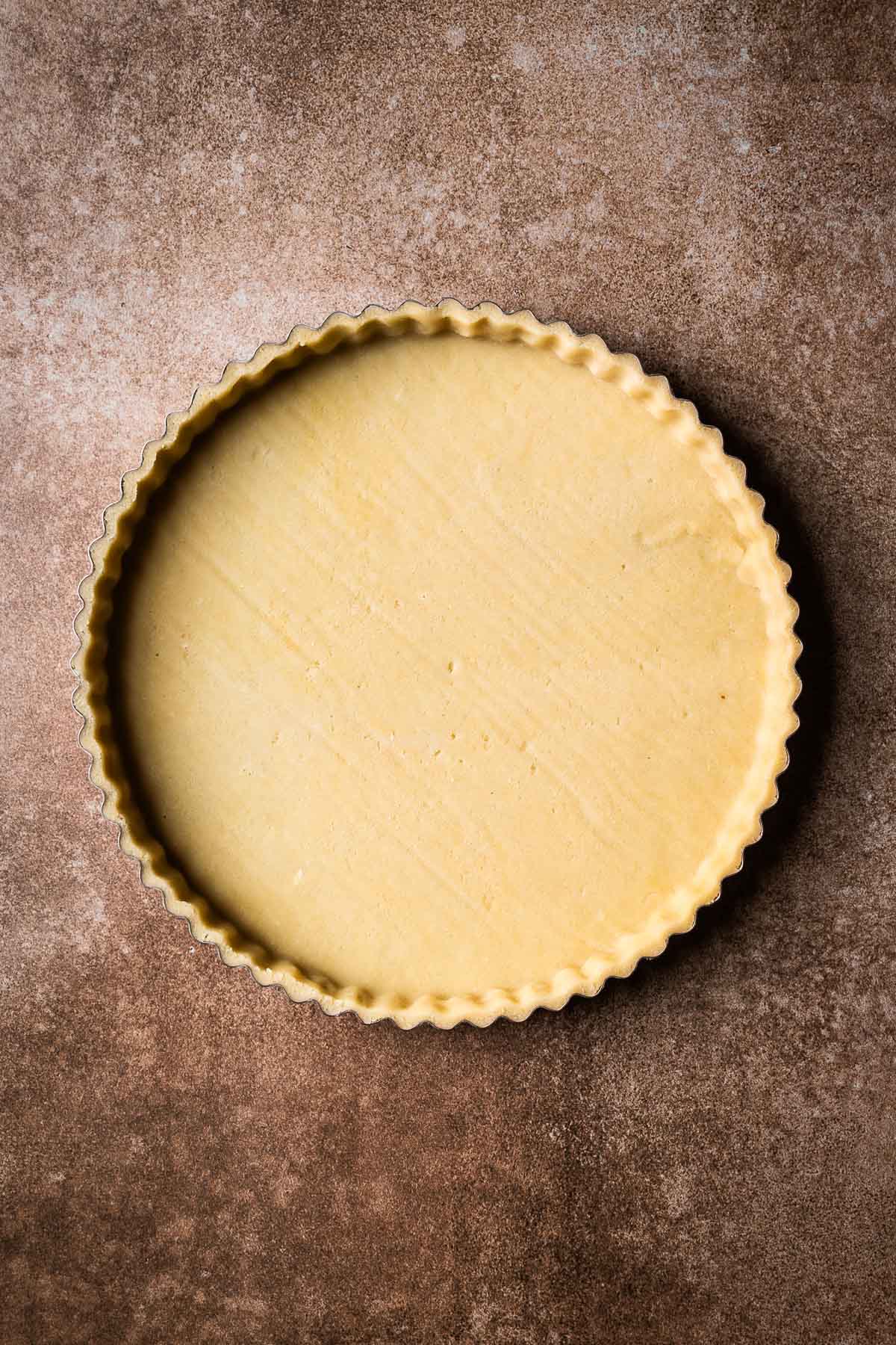 Unbaked pate sucree tart dough in a fluted metal pan.
