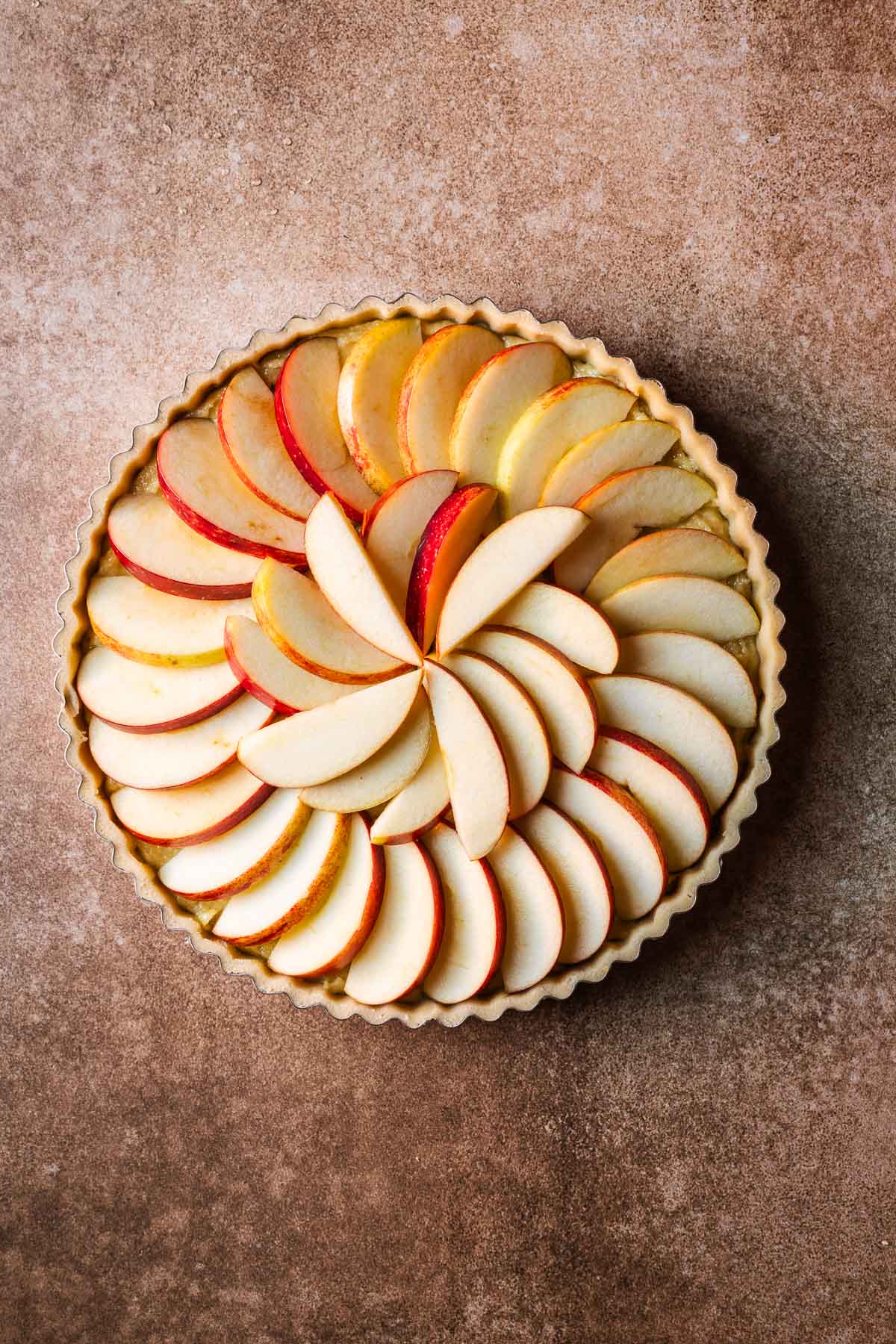 A round unbaked tart topped with overlapping concentric circles of apple slices.