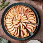 A round apple tart on a dark green serving plate with two slices cut.