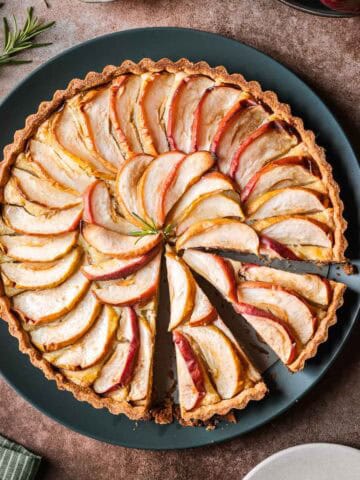 A round apple tart on a dark green serving plate with two slices cut.