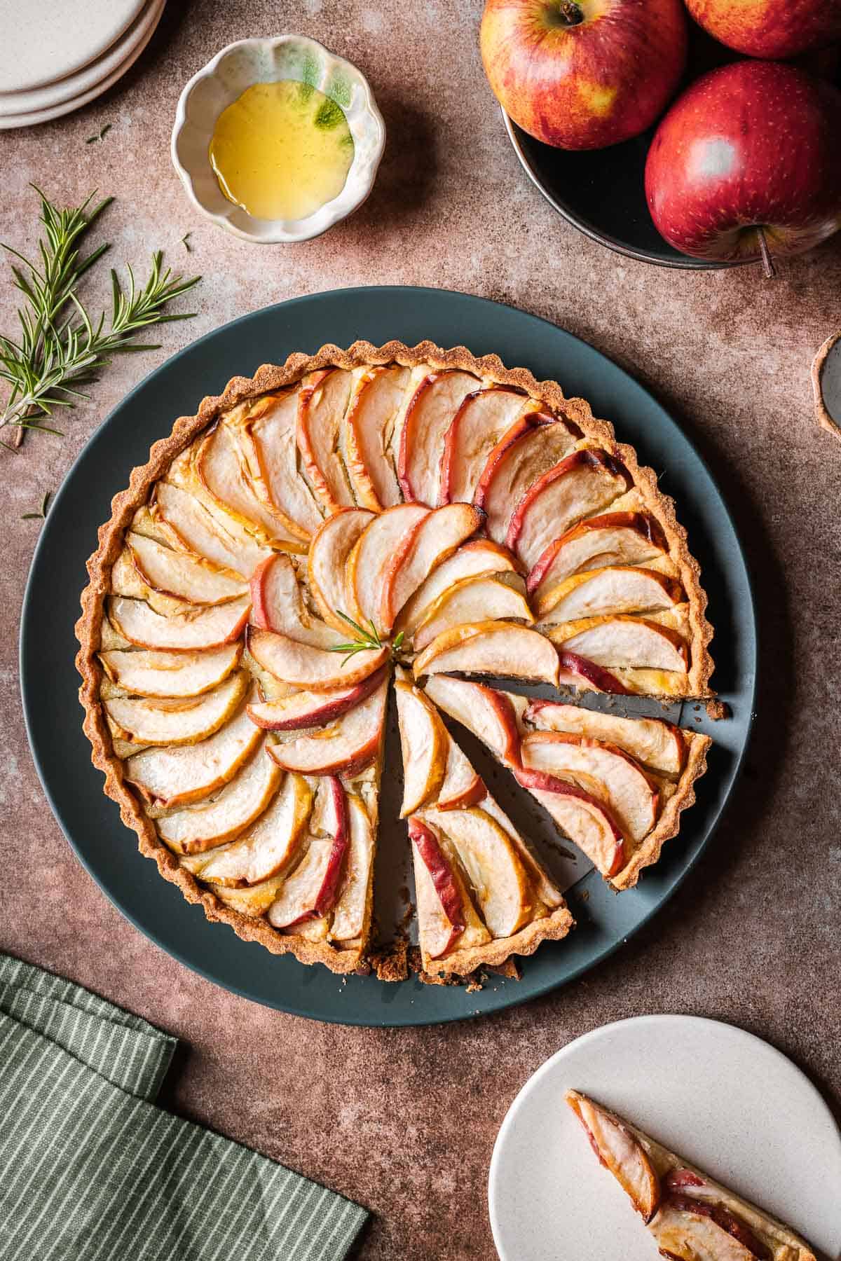 A round apple tart on a dark green serving plate with two slices cut.