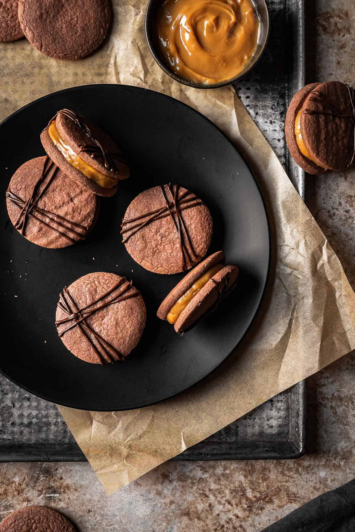 Chocolate sandwich cookies filled with dulce de leche on a black plate.