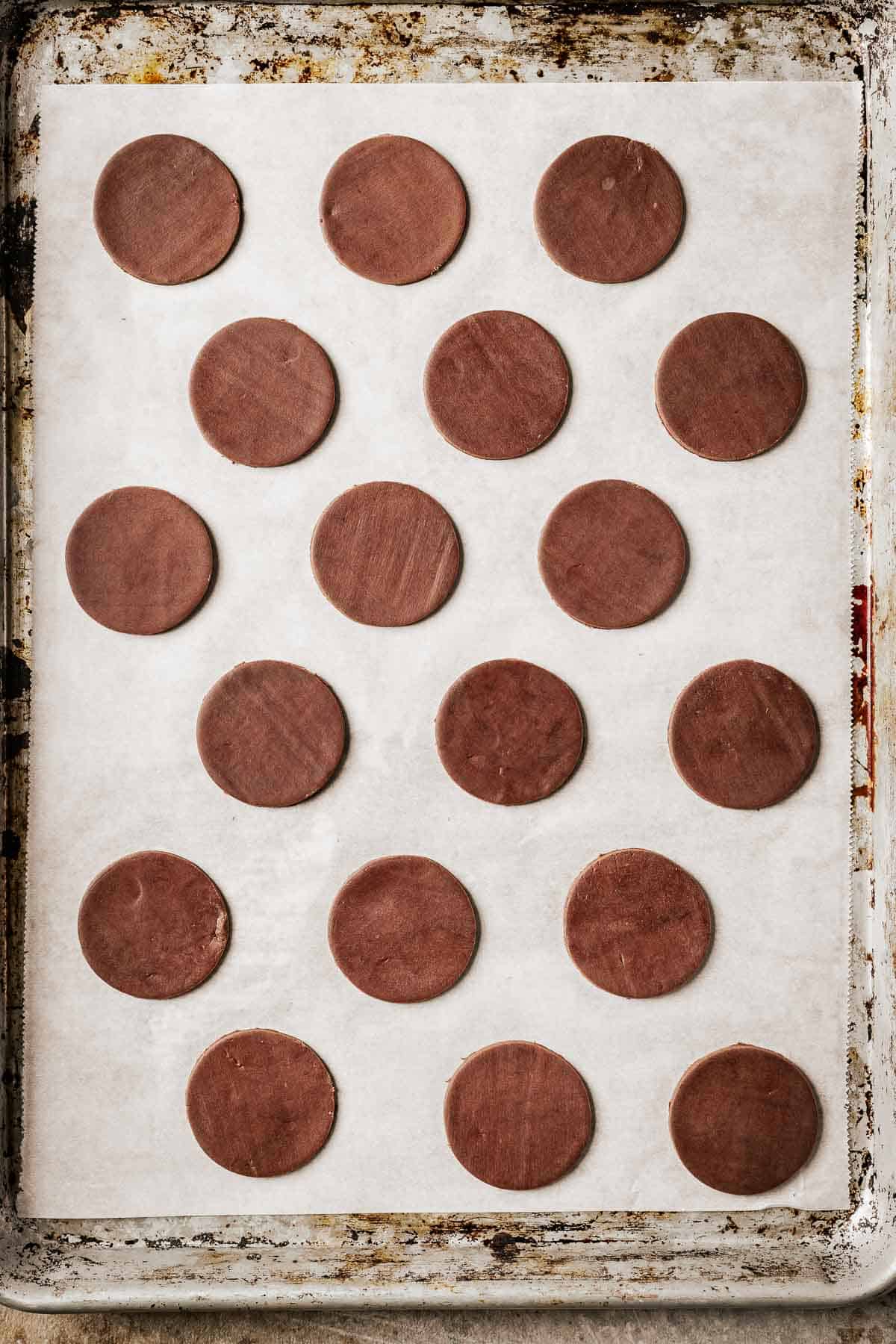 Chocolate cookie dough circles on a parchment lined baking sheet.