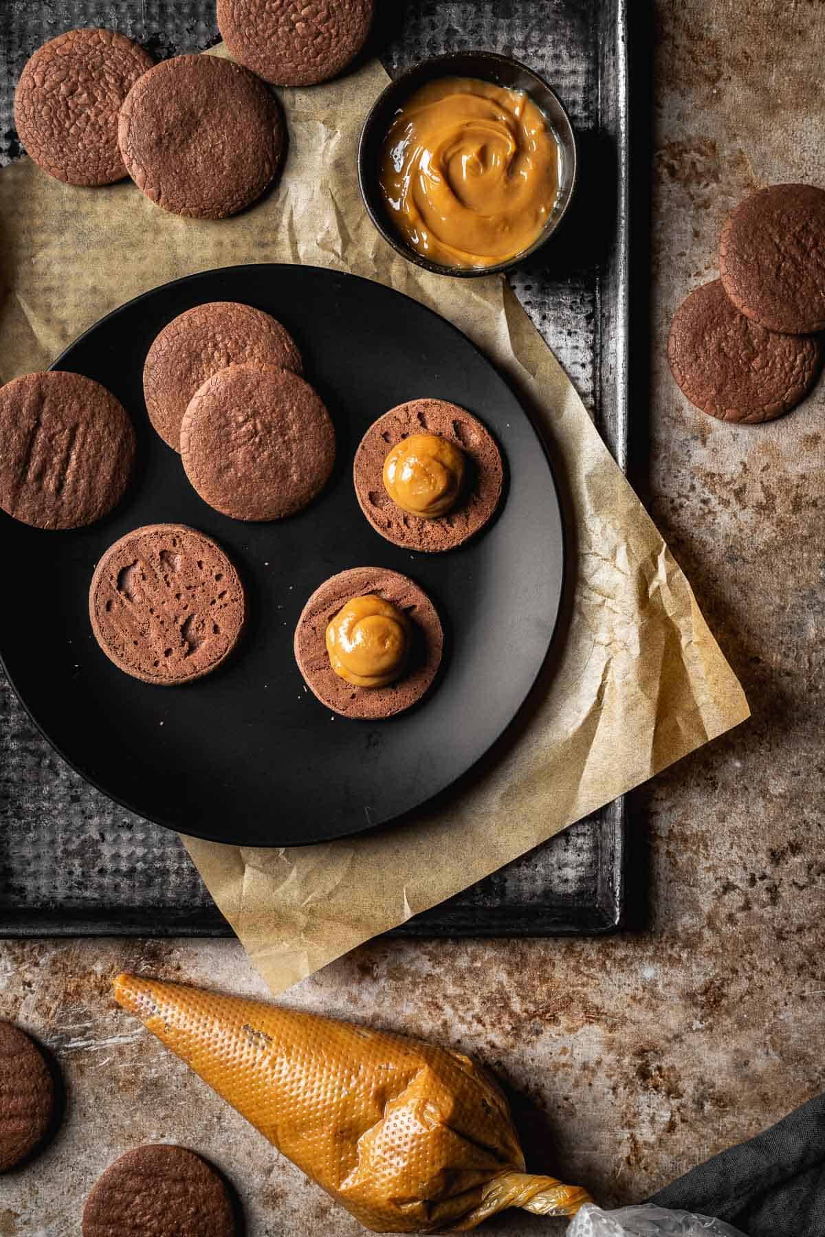 Cookies filled with dulce de leche and a piping bag of dulce de leche.